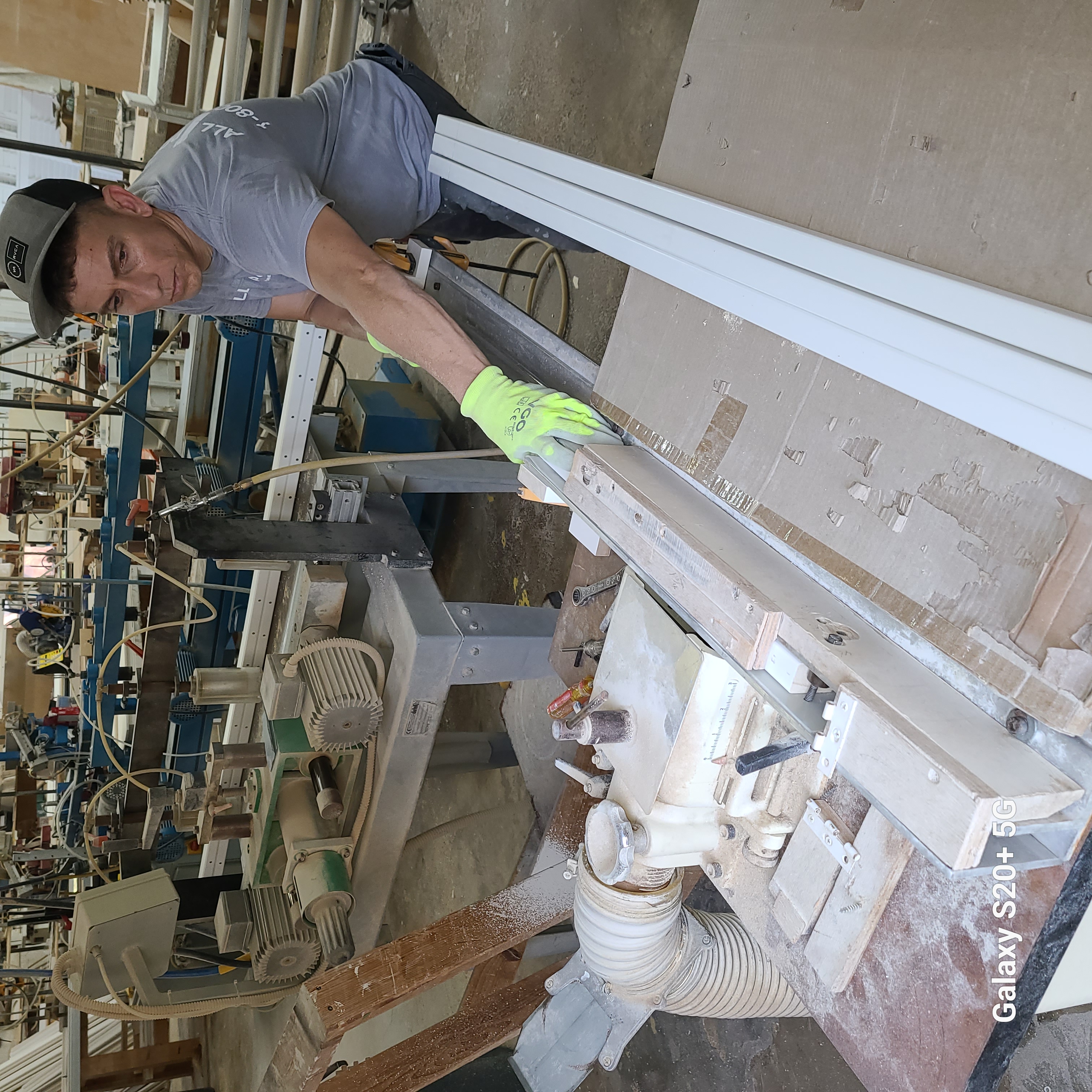 Craftsman handling long white shutter components at a workshop bench fixture