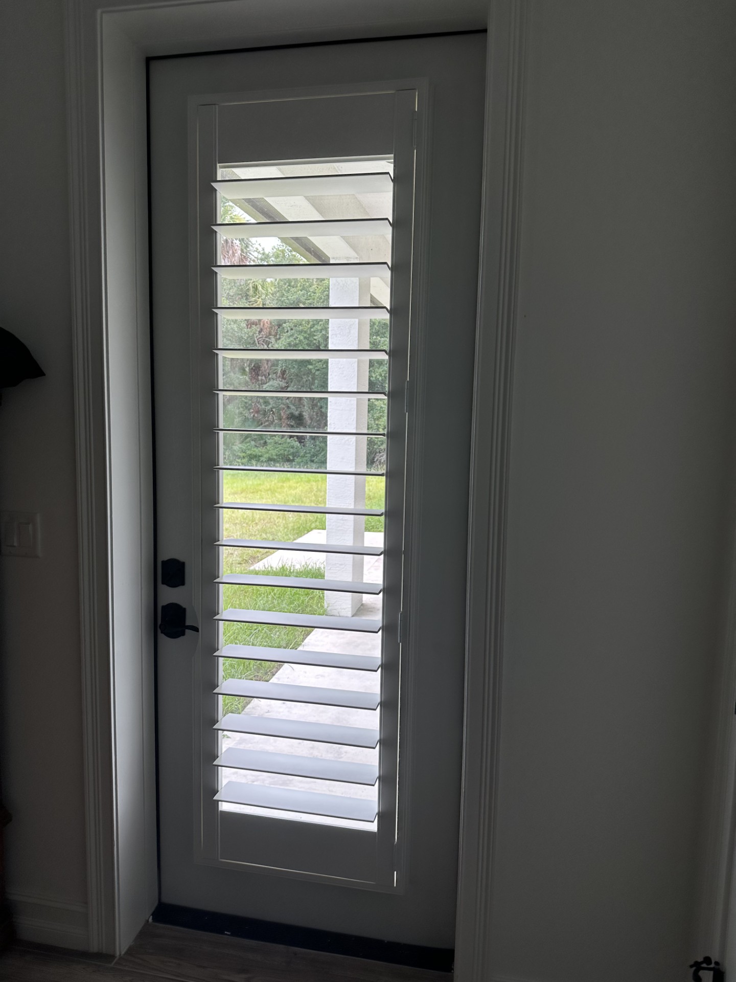 White single patio-door shutter with open louvers, a subtle curved handle clearance and no center tilt rod