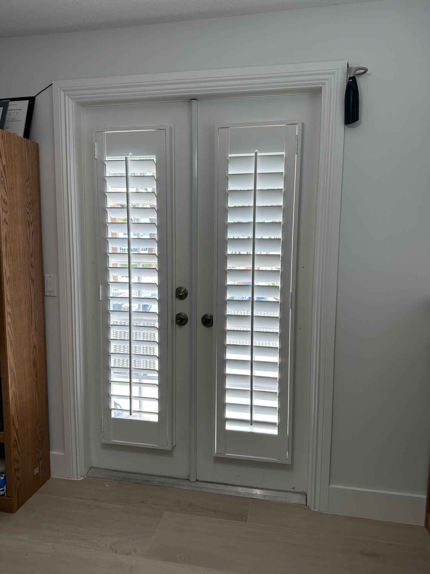 Narrow white shutters on double glass doors with straight frames and exposed door knobs