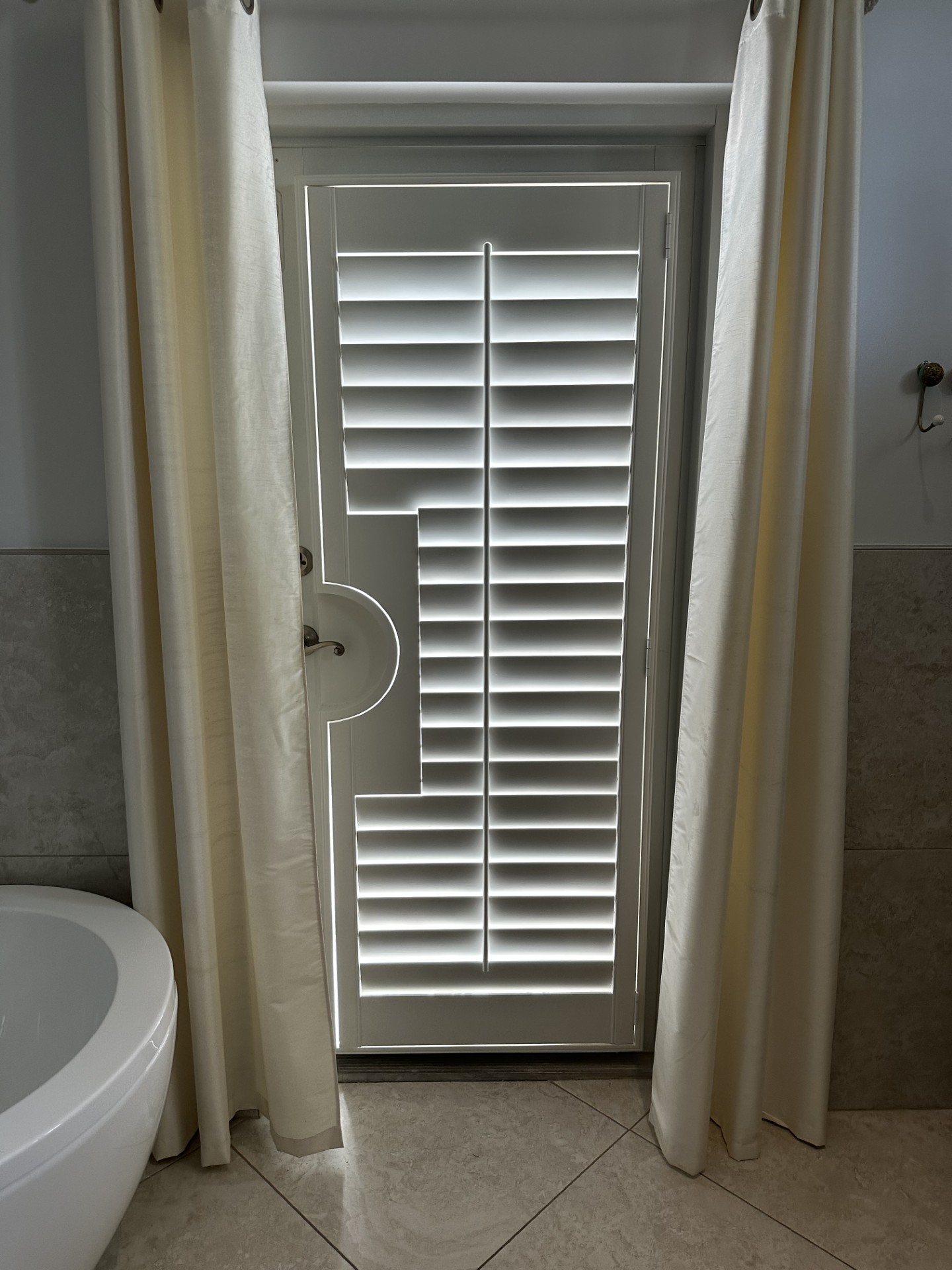 White bathroom door shutter with a rounded cutout beside a lever handle