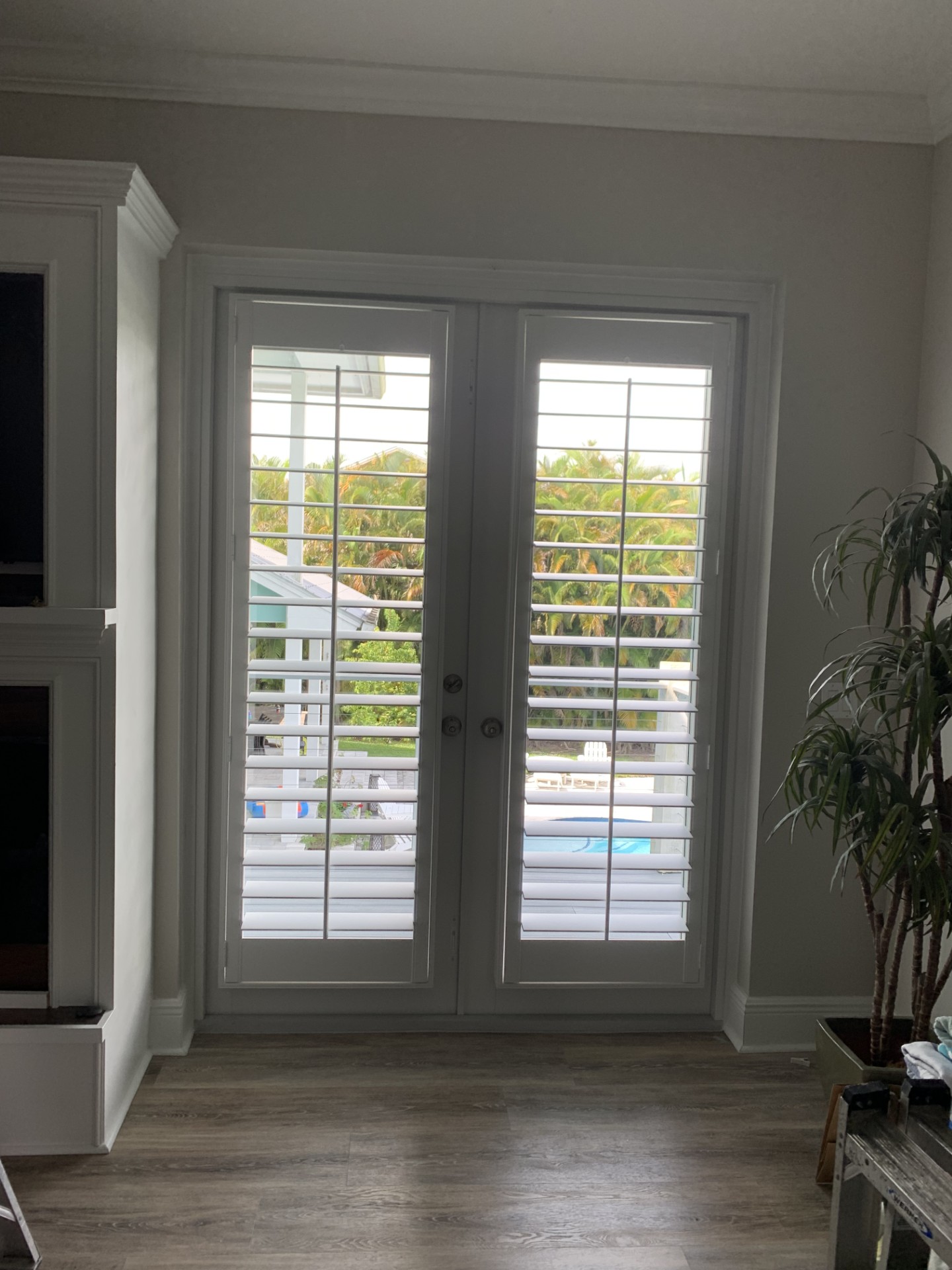 White plantation shutters on double French doors with louvers open toward a patio