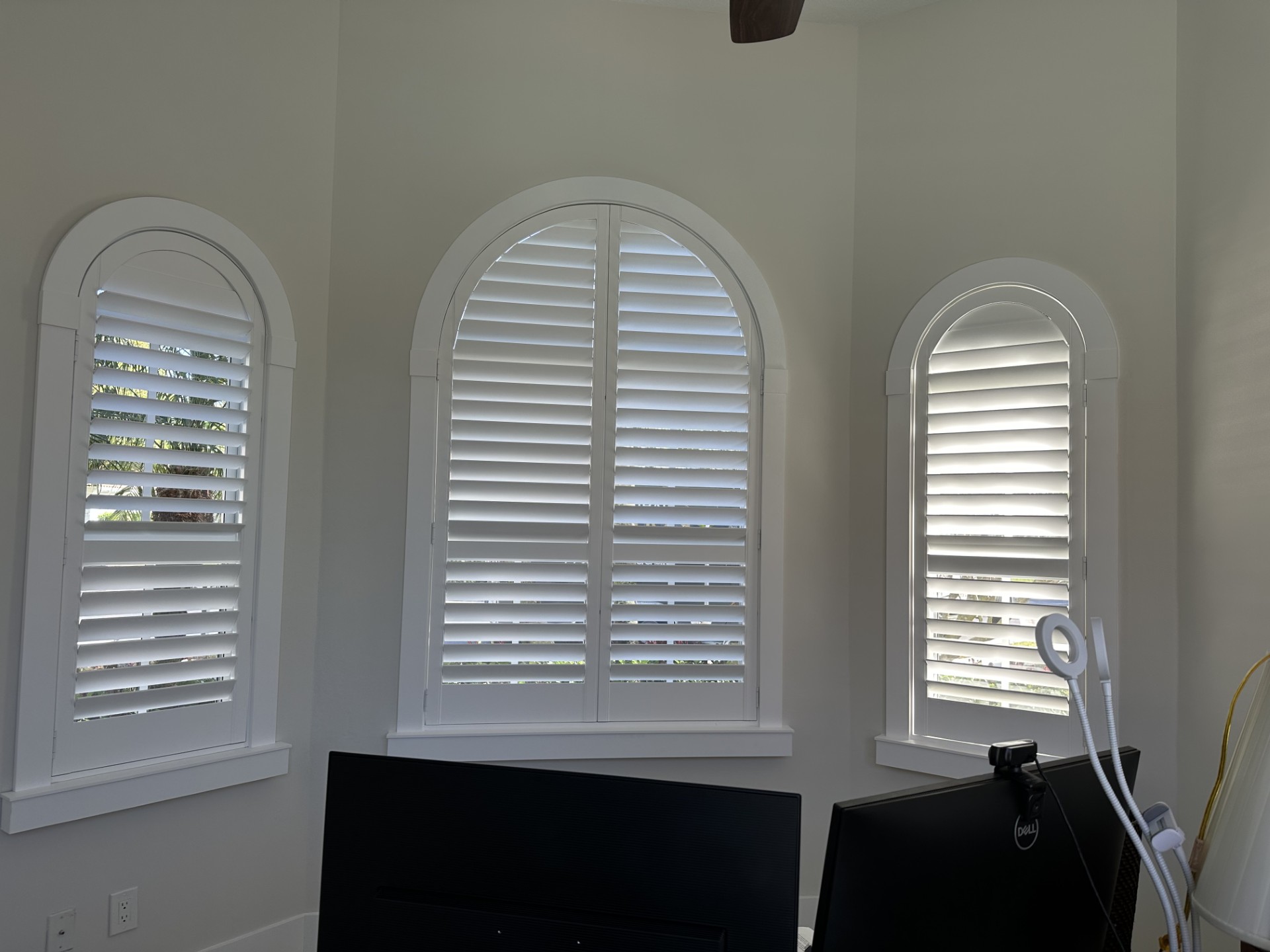 Three separate arched windows fitted with white plantation shutters in a home office