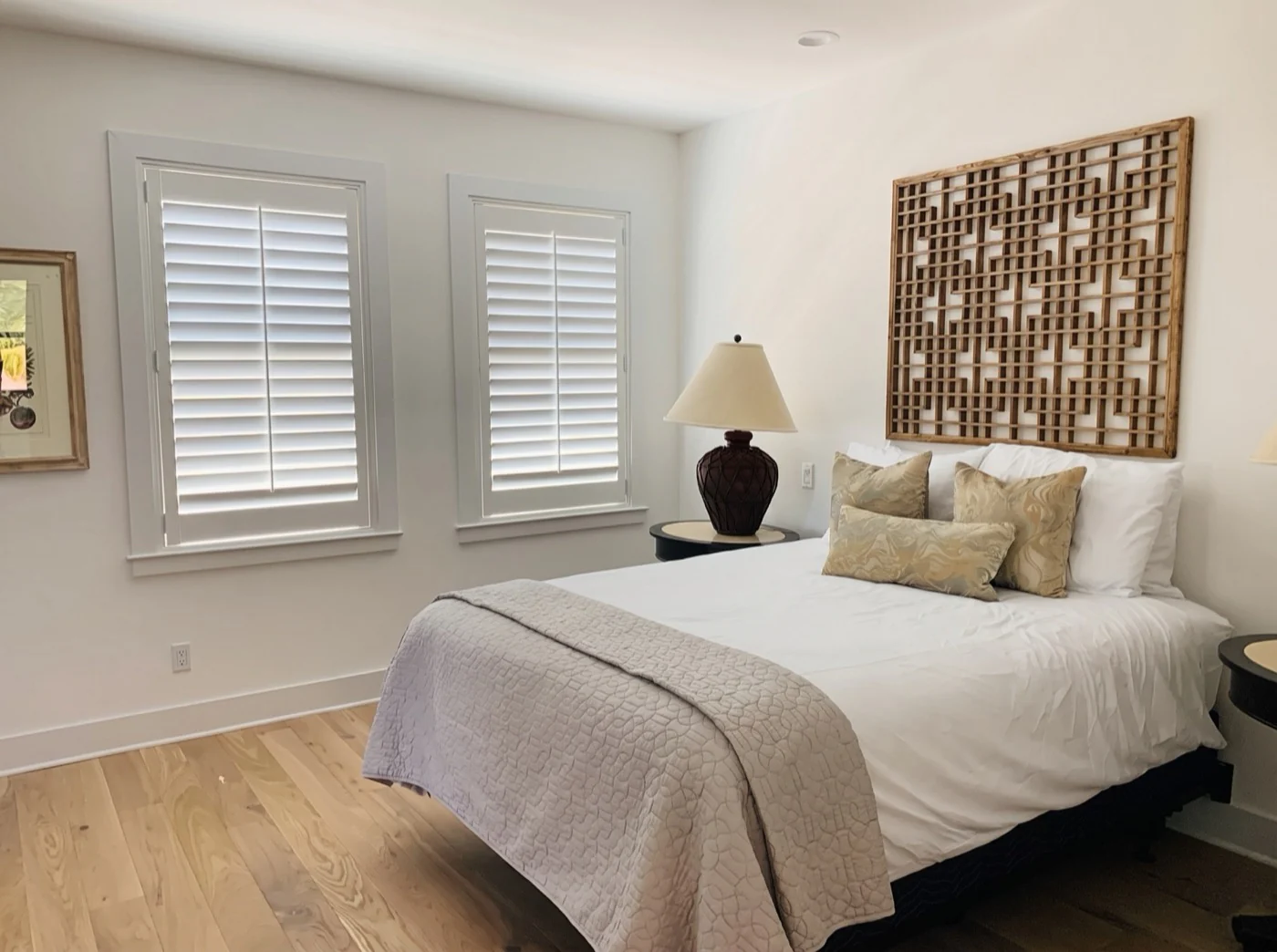 White plantation shutters framing the windows in a bright bedroom