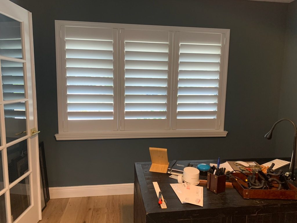 Three-panel plantation shutter fitted to a wide window in a home office, Stuart, FL
