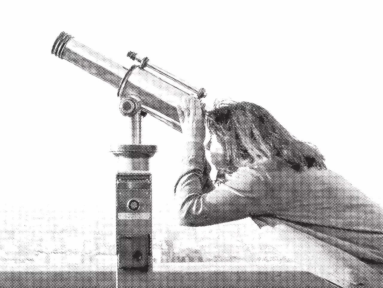 Person looking through a mounted telescope by a railing.