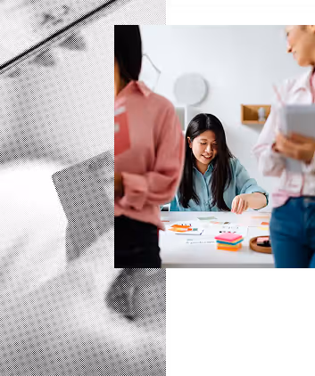 Three women collaborating at a table with sticky notes and papers, one woman smiling and writing.