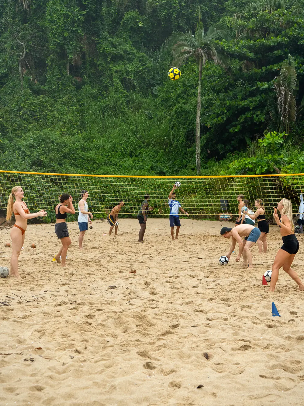 Group playing footvolley on the beach under a net, jungle backdrop