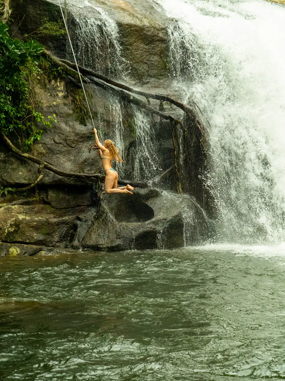 Woman swinging off a rope into the pool below a waterfall