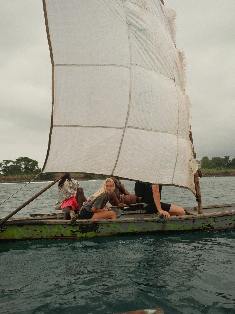 Group sailing on a traditional wooden boat with a patched canvas sail