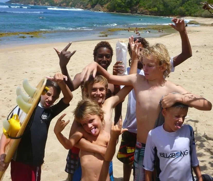 A group of young surfers on a Martinique beach, Fayed among them, pulling faces for the camera.