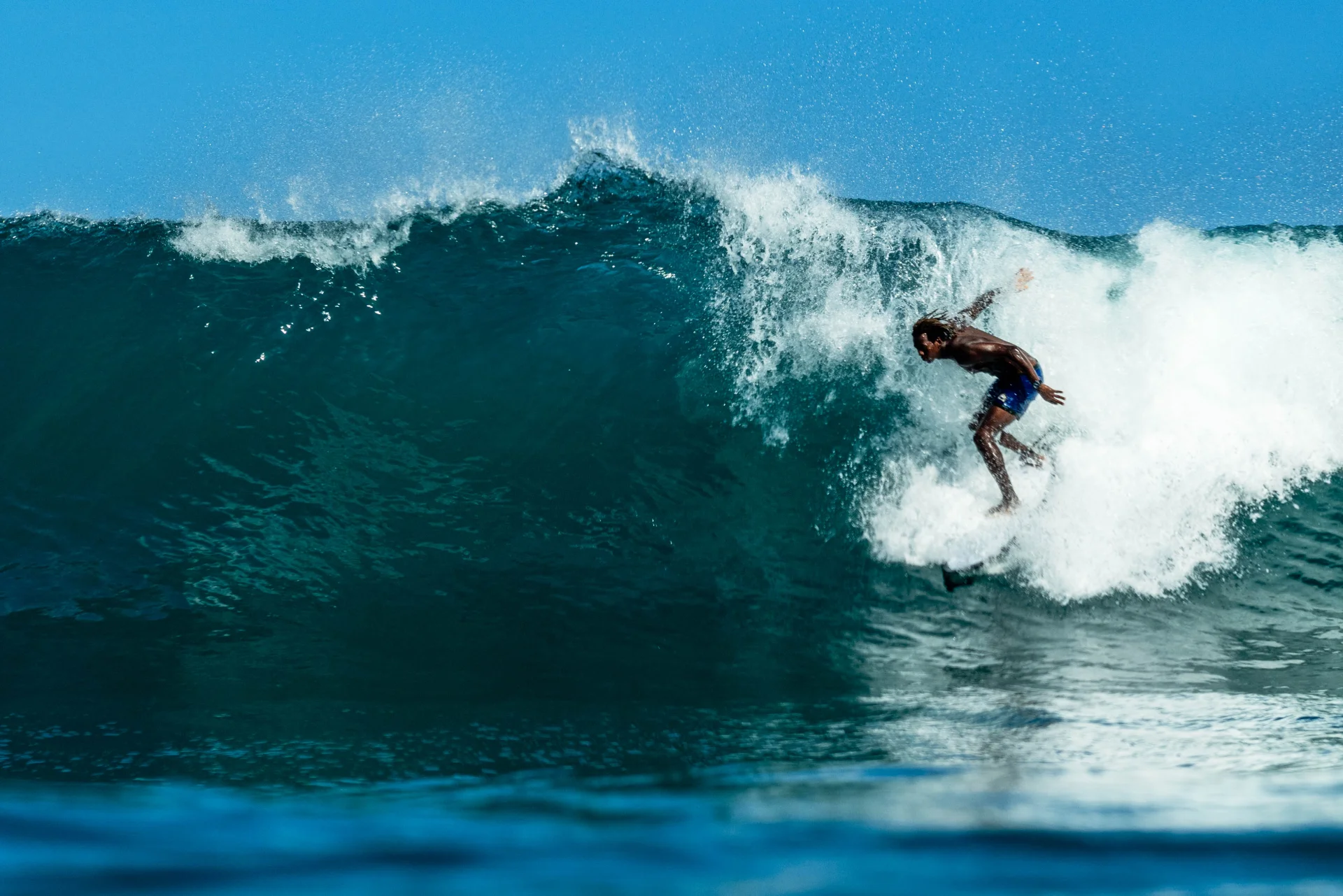 Fayed on a clean blue wave, driving off the bottom with spray behind him.