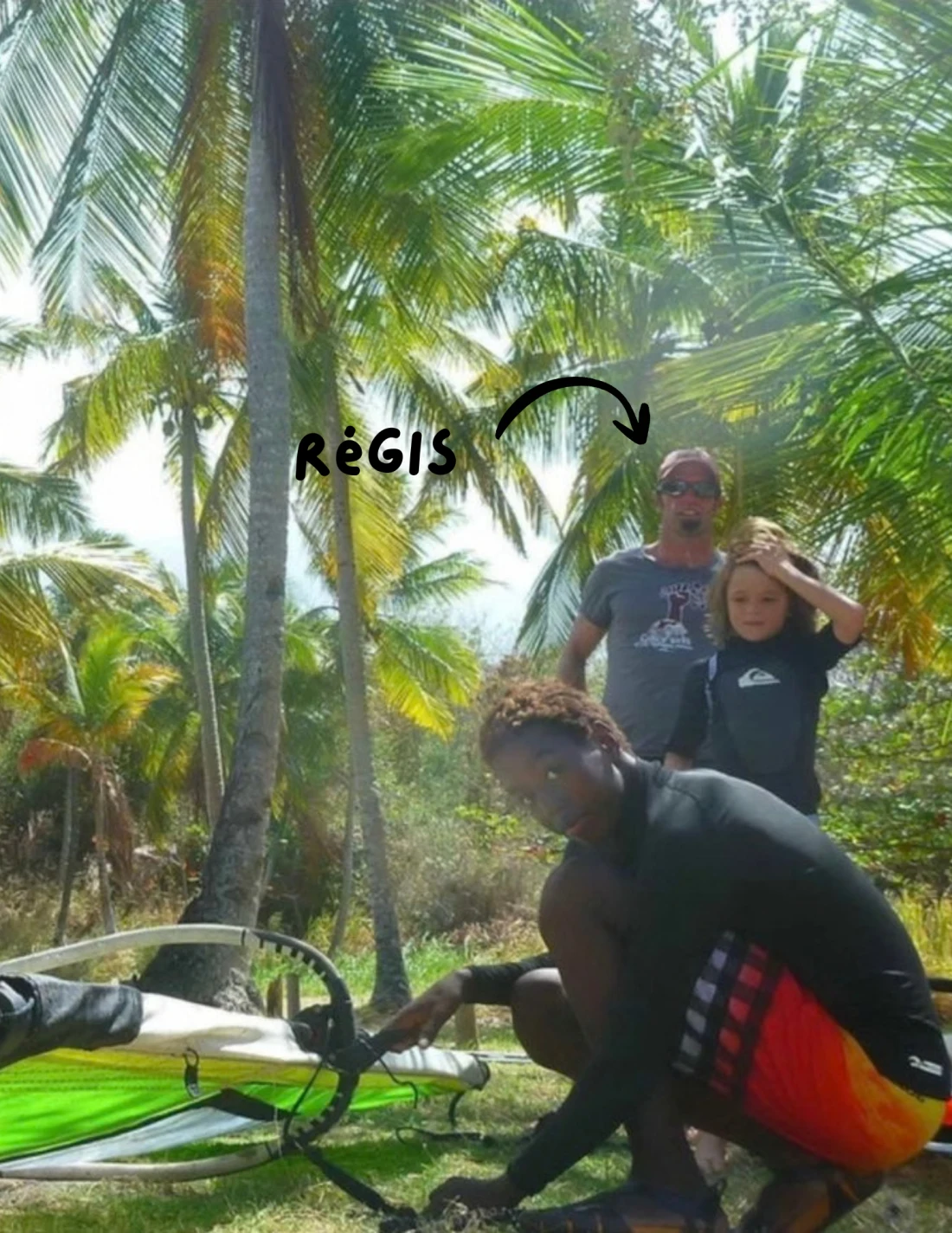 Fayed kneeling over a rigged sail under the coconut palms in Martinique, with a handwritten arrow labelled Régis pointing to Régis Mengual standing behind him.