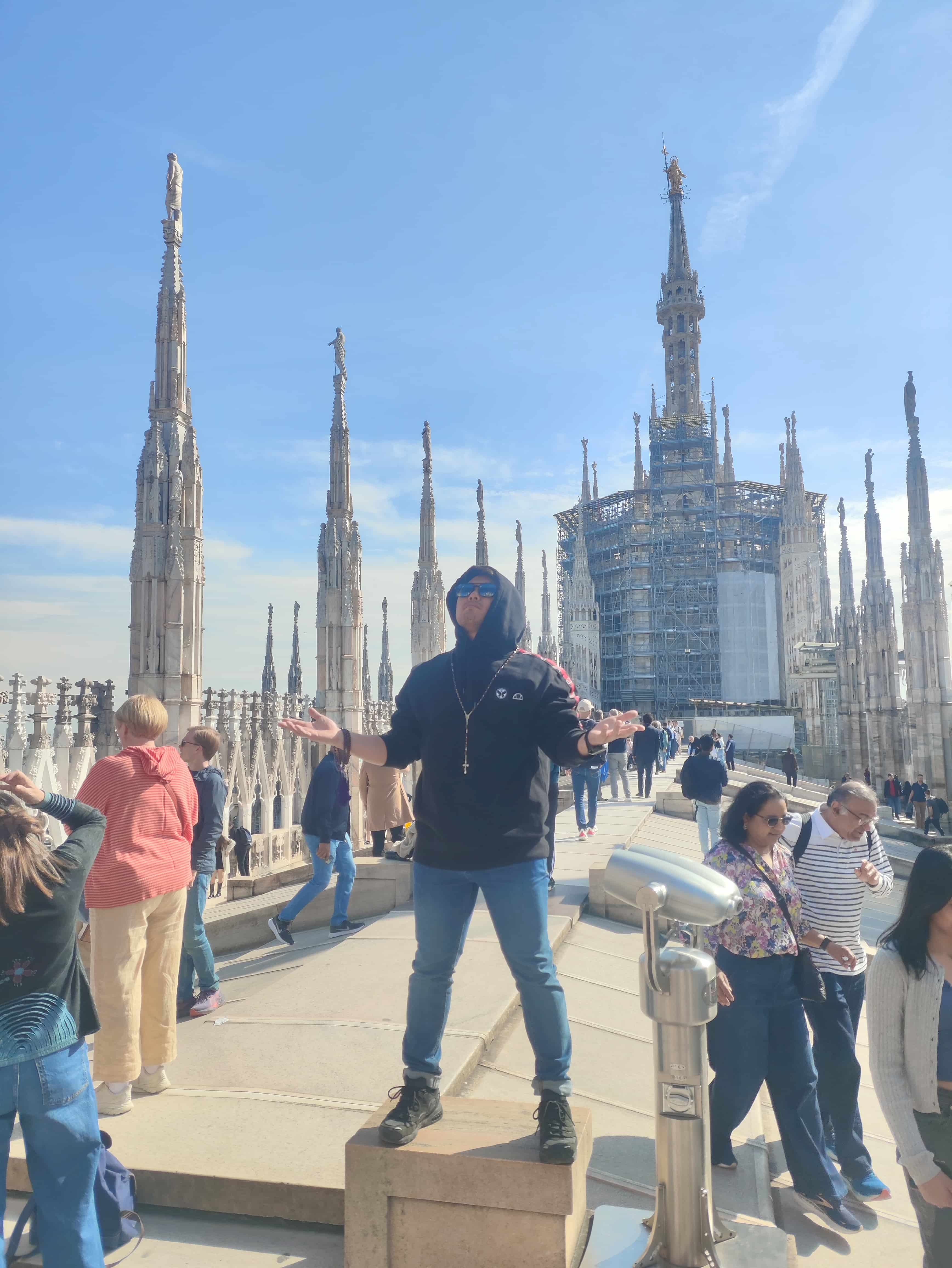 Kazu debout devant la cathédrale du Duomo de Milan en Italie, bras ouverts dans une posture de prière.