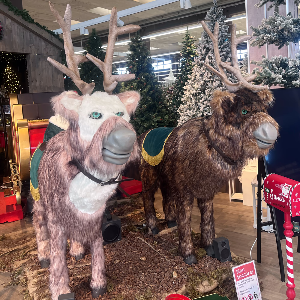 Cometa e Cupido installate in centro commerciale con bardature decorative dorate e verdi, creando esperienza natalizia immersiva tra alberi illuminati