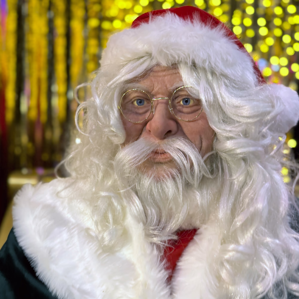 Primo piano Santa Claus con barba realistica e occhiali, illuminazione dorata atmosferica evidenziando qualità artigianale della figura scenografica Menart.