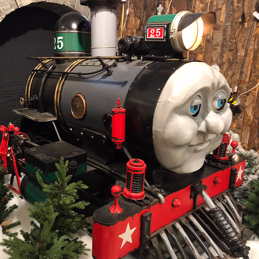 Tommy Express, locomotiva scenografica Menart con volto animato e occhi LED blu, installata in tunnel di pietra con dettagli realistici per esperienza ferroviaria magica.