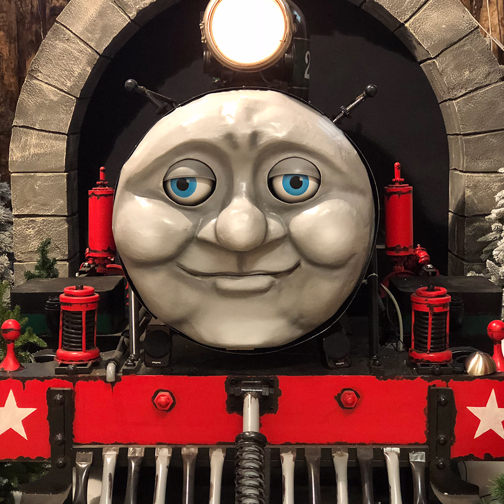 Primo piano Tommy Express evidenziando dettagli artigianali del volto sorridente con occhi LED blu e illuminazione tunnel, mostrando qualità scenografica Menart.