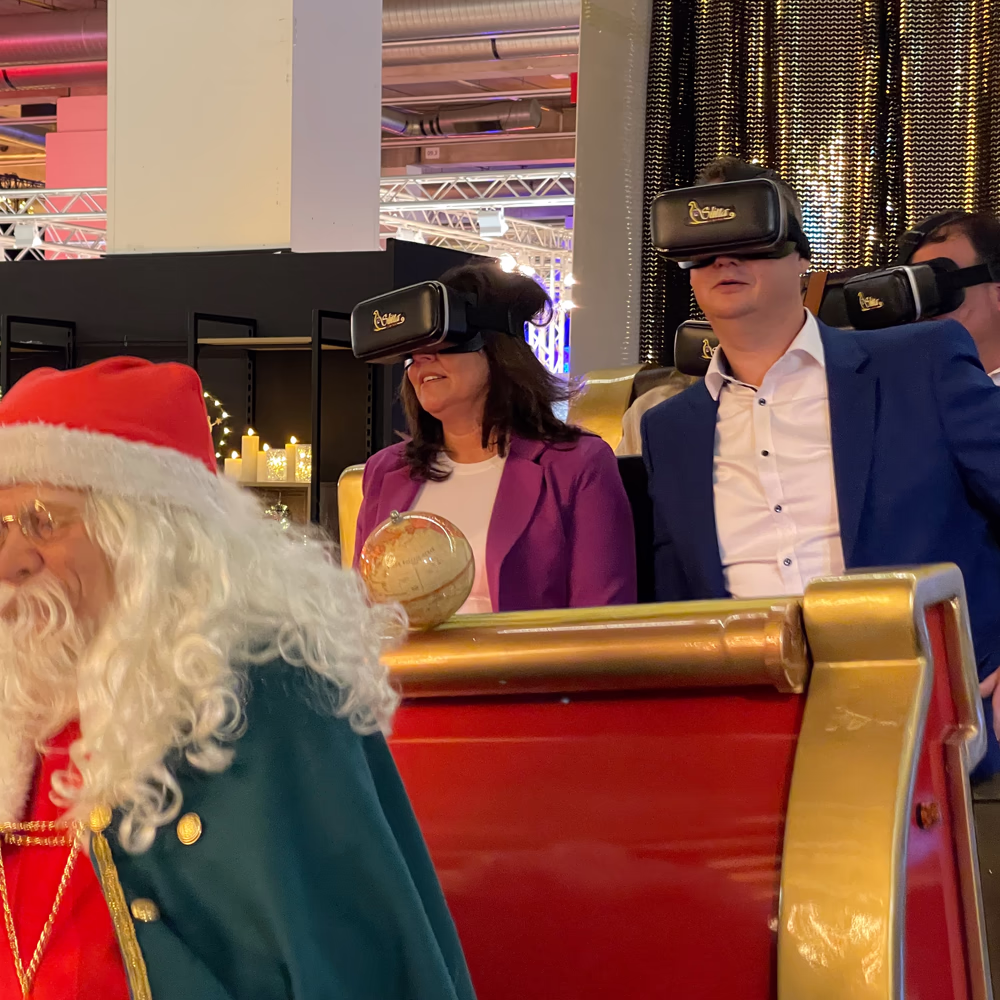 Adulti utilizzano visori VR su Slitta Express dorata con Santa Claus, dimostrando esperienza immersiva natalizia tecnologicamente avanzata in ambiente espositivo moderno.