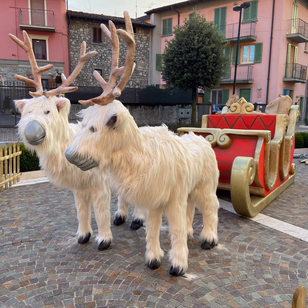 Renne scenografiche bianche con slitta rossa e dorata di Chi Ha Incastrato Santa Claus, allestimento Menart su pavimentazione storica per esperienza natalizia urbana immersiva.