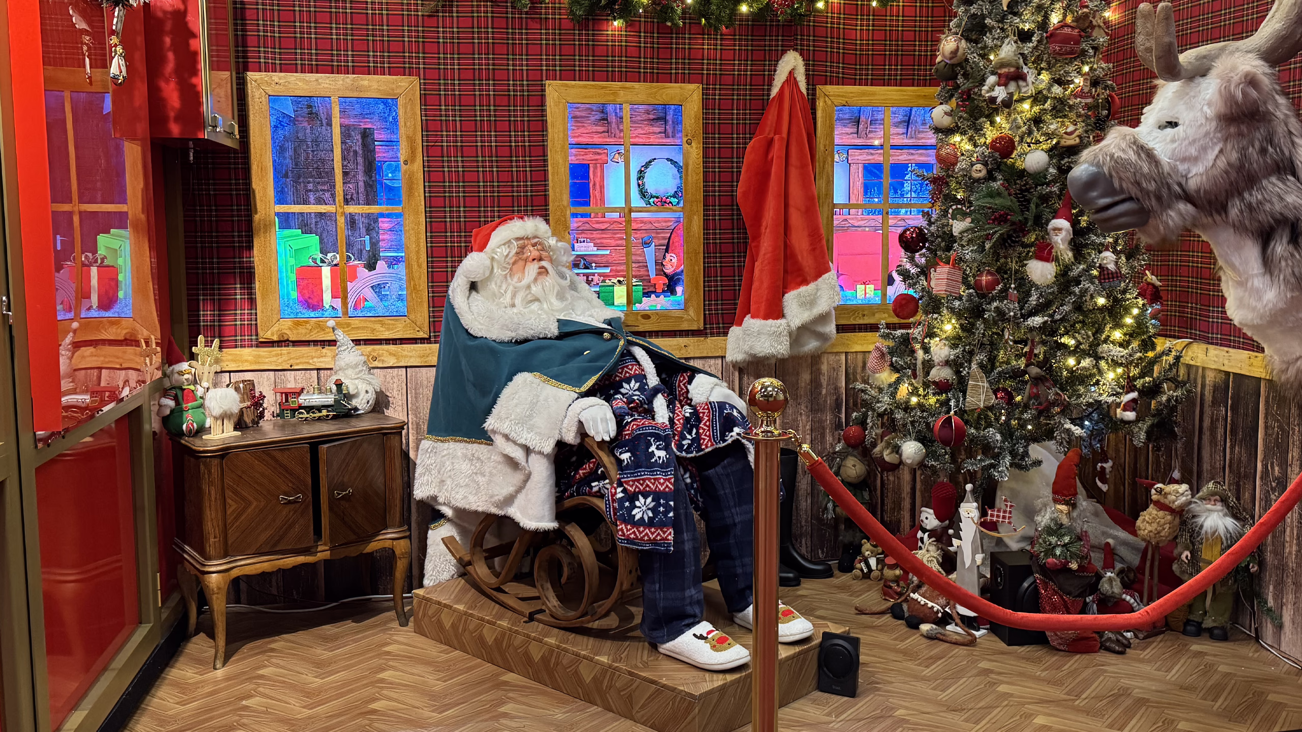 Santa Claus's magical bedroom with animated digital windows, plaid fabrics and warm lighting, creating an immersive Christmas experience for shopping malls.