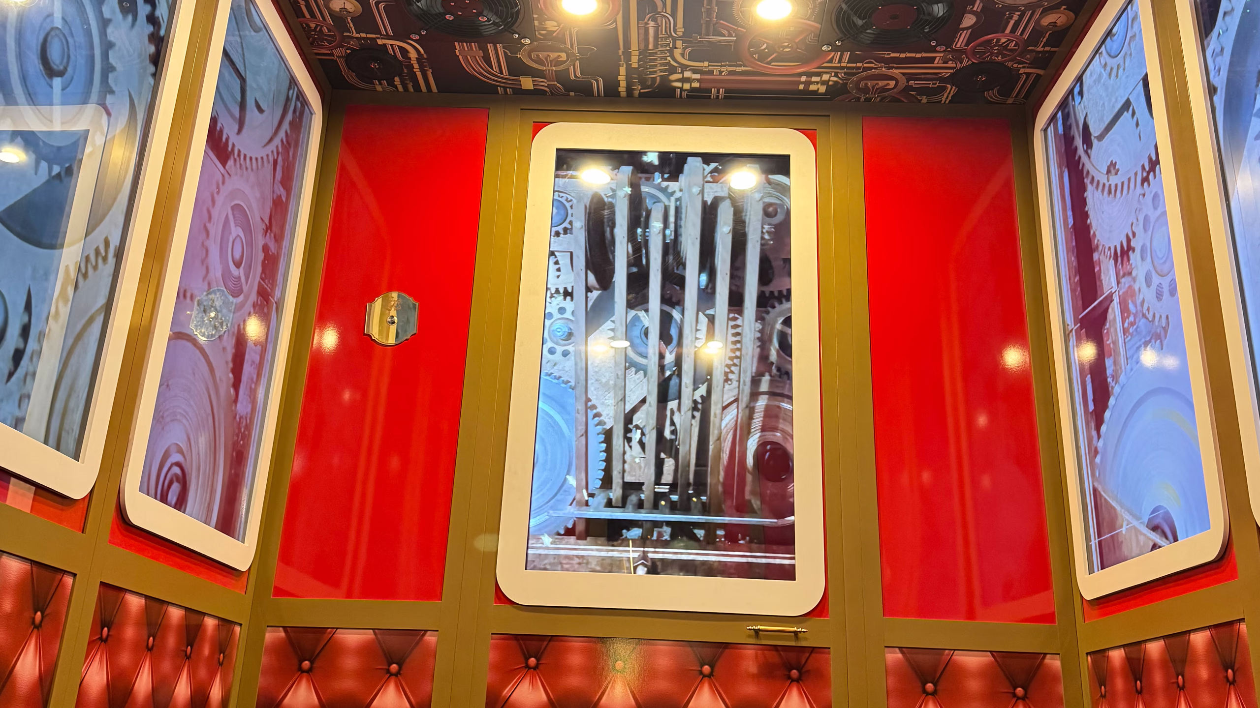 Magic Elevator by Menart with visible illuminated mechanisms, gold finishes and decorative red panels, creating an immersive steampunk scenographic experience for shopping centers.