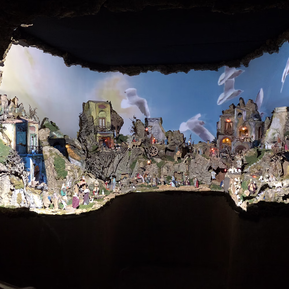 Nativyx - Piccolo, presepe scenografico multimediale Menart con villaggio in miniatura, luci integrate e videoproiezione di cieli in movimento; materiali artigianali e mapping creano atmosfera immersiva, teatrale e contemplativa.