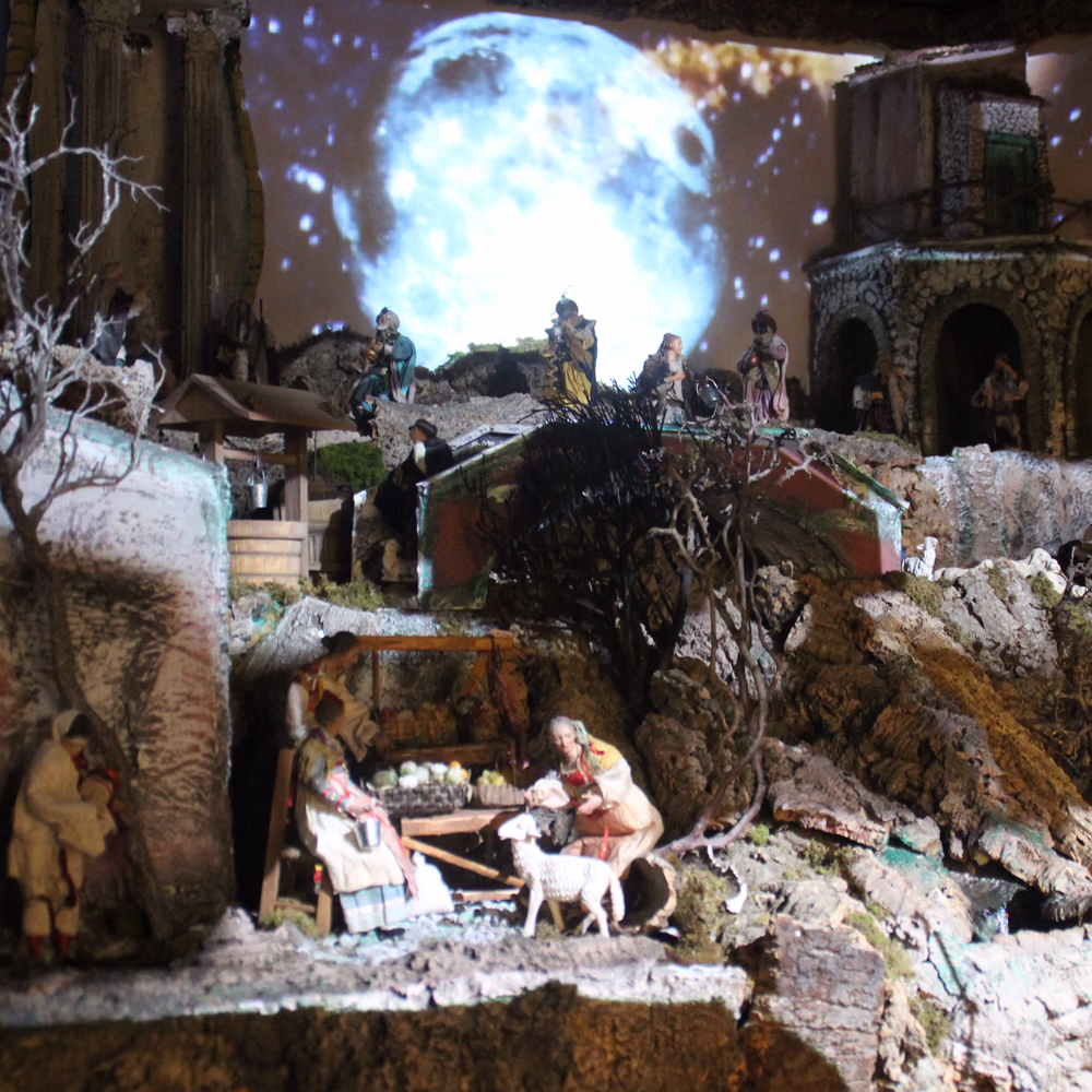 Nativyx - Medio, presepe scenografico multimediale Menart con miniature artigianali, fondali in sughero e pietra, videoproiezione lunare e luci integrate; videomapping e audio immersivo creano atmosfera notturna poetica e contemplativa.