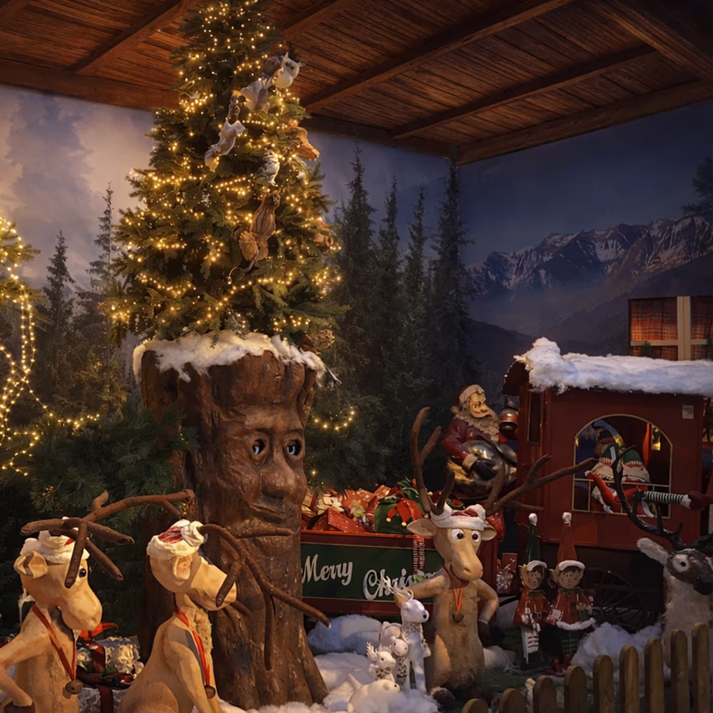Illuminated Christmas tree with human face and reindeer with Santa Claus hats in snowy scene.