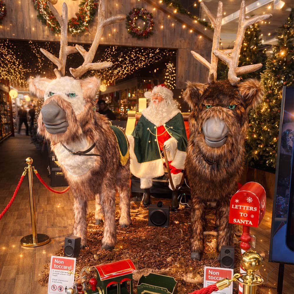 Babbo Natale seduto su una slitta trainata da due renne finte in un ambiente decorato con luci natalizie.