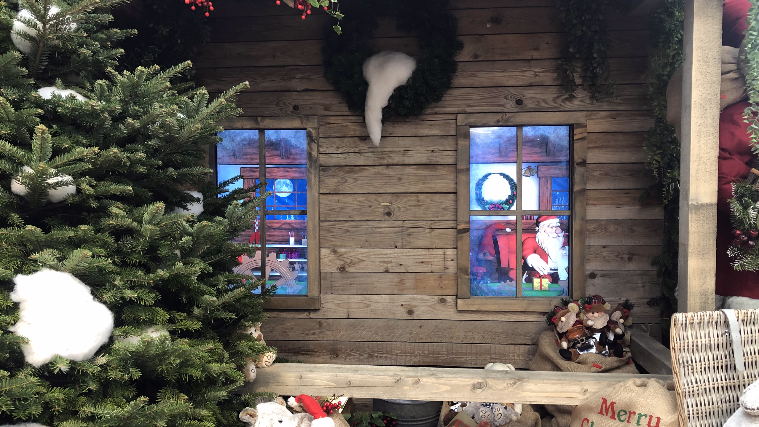 Le Finestre su una casetta di legno natalizia, con Babbo Natale animato in 3D in uno dei due schermi accanto all’albero