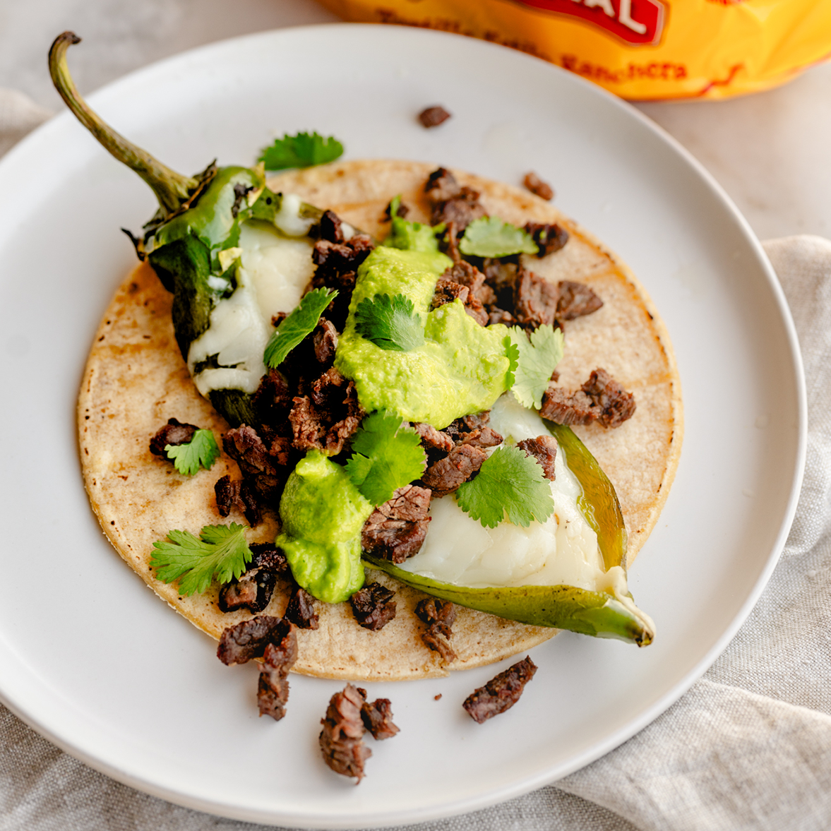 Corn tortilla package and taco with seasoned meat, cilantro, and roasted pepper