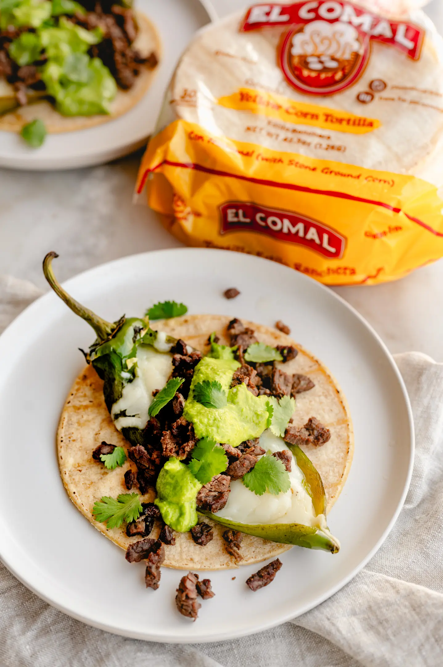 Corn tortilla package and taco with seasoned meat, cilantro, and roasted pepper