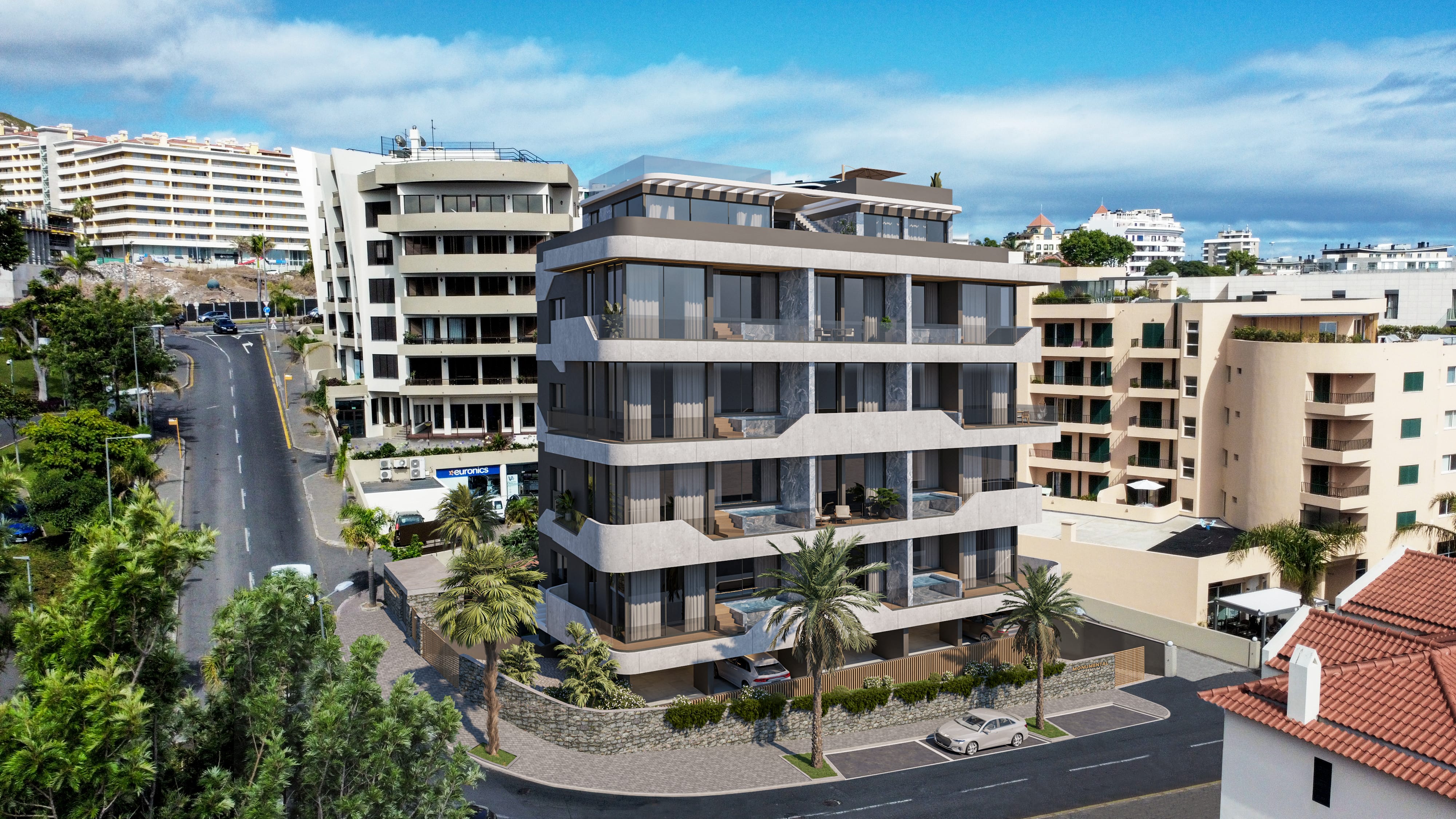 Complexo de apartamentos com design moderno e curvo, situado numa paisagem urbana montanhosa. O edifício tem grandes varandas de vidro, uma fachada de cores claras e escuras e está rodeado por outros prédios, vegetação e estradas.