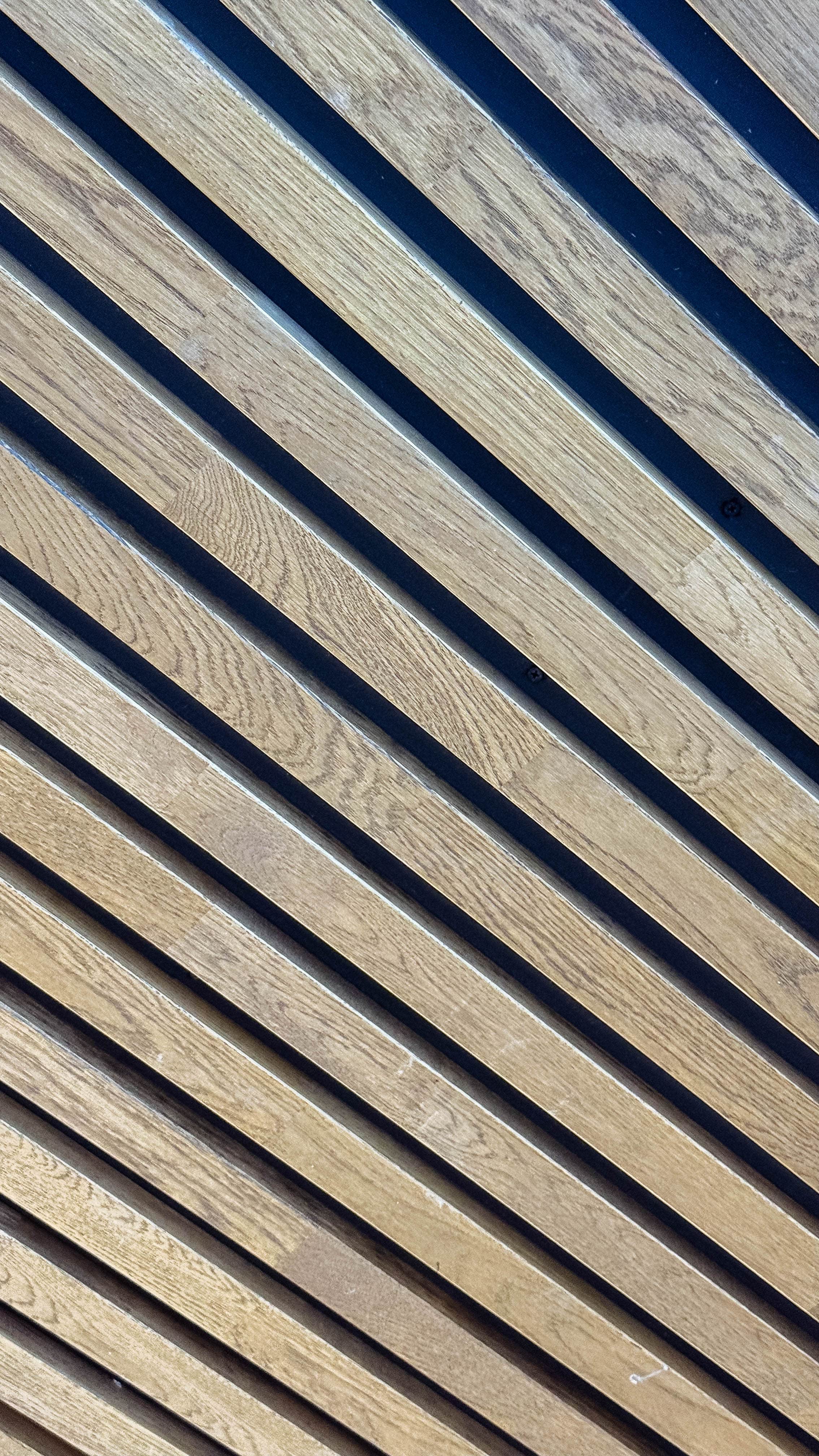 Close-up de uma superfície de madeira clara com ripas diagonais, criando um padrão texturizado com sombras contrastantes.