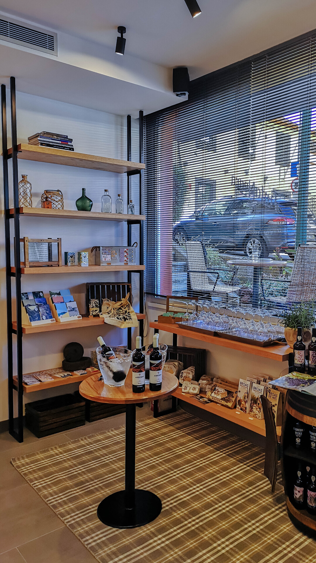 Esquina do Tinta Negra Wine Bar, com uma janela para o exterior e prateleiras de madeira com produtos expostos e elementos decorativos.