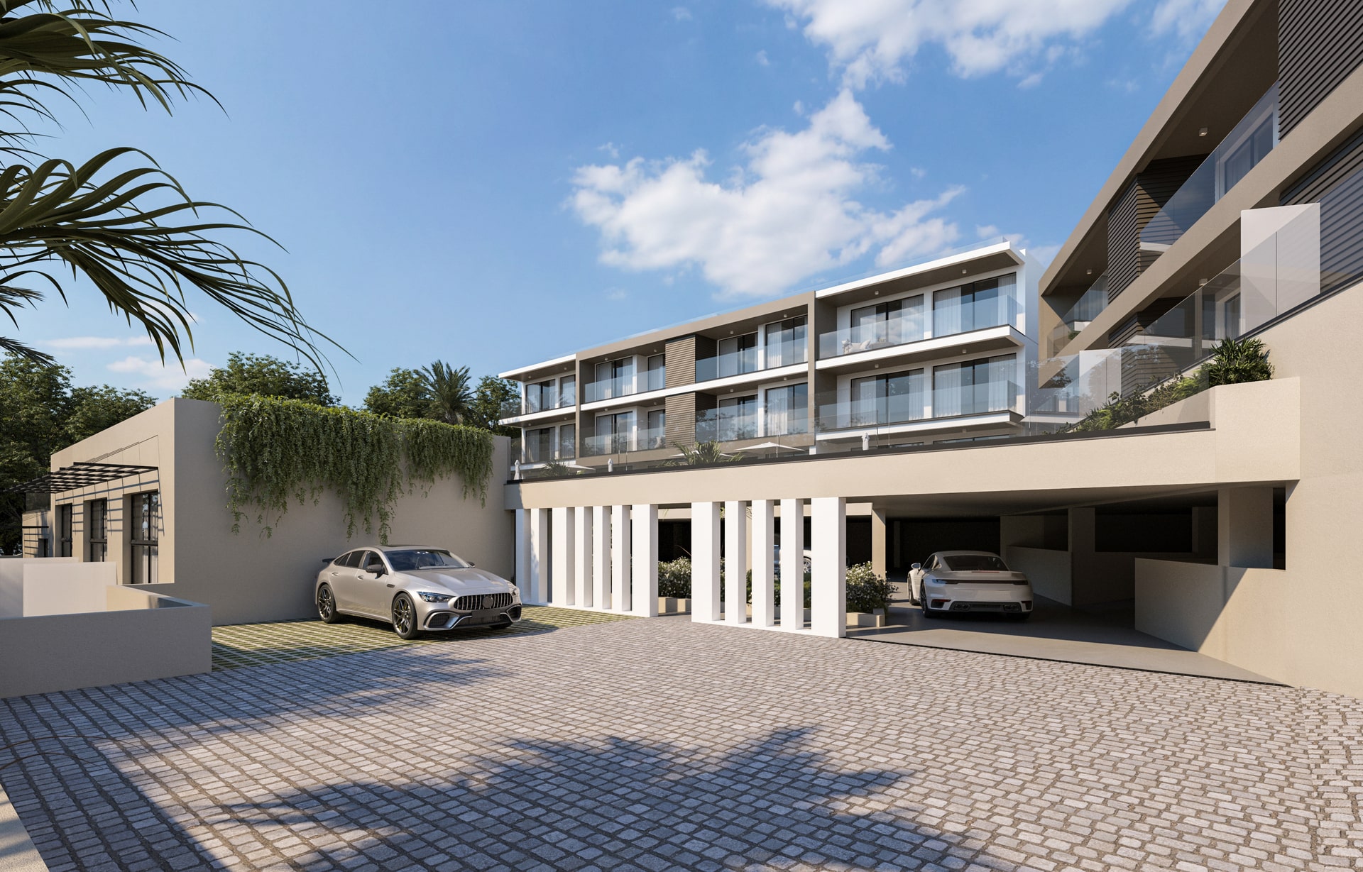 Um edifício residencial de design moderno, com grandes varandas de vidro, fachada de cor clara e detalhes em cinza escuro. A propriedade possui uma garagem de estacionamento coberto e uma área de entrada com um pátio de pedras. A paisagem inclui vegetação.