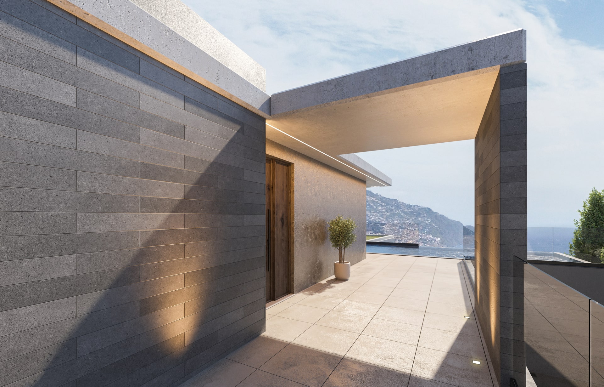 Fachada de casa moderna com parede de pedra cinza, área externa com vista para o mar e céu azul, e árvores ao fundo