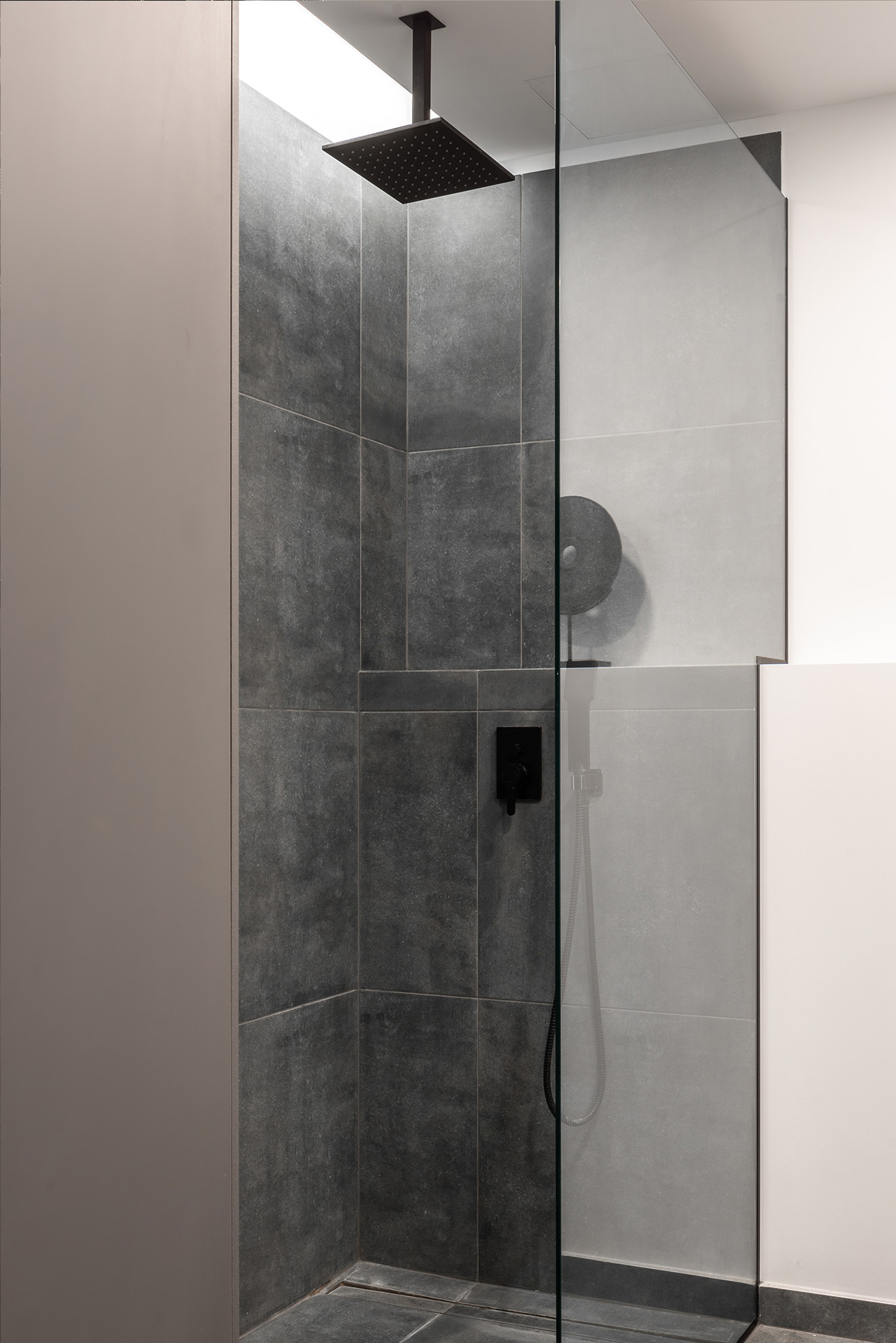 Walk-in shower with dark grey tiles and matte black rain shower — interior by TOMA Studio