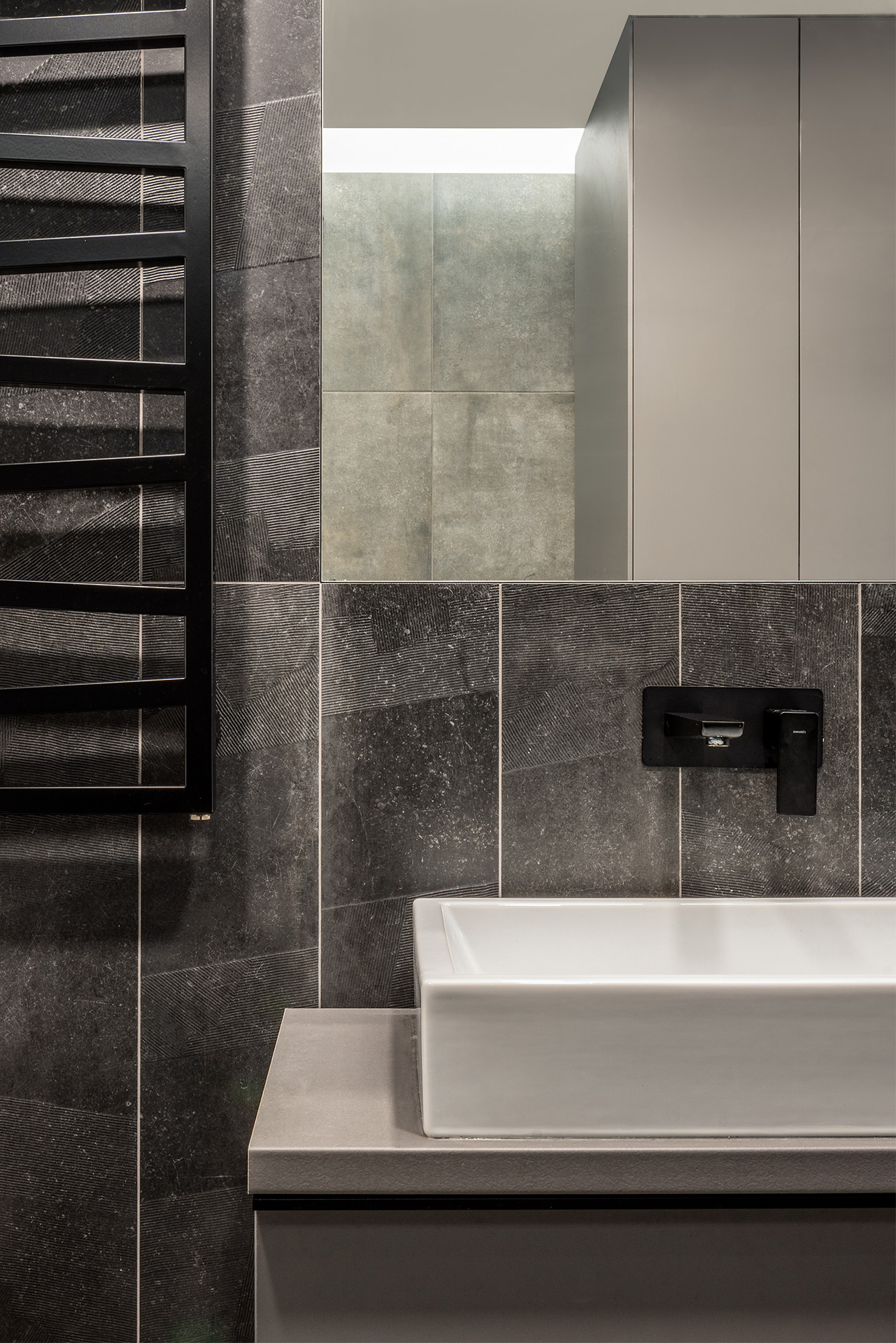 Close-up of washbasin area with textured dark tiles and mirror reflection — interior by TOMA Studio