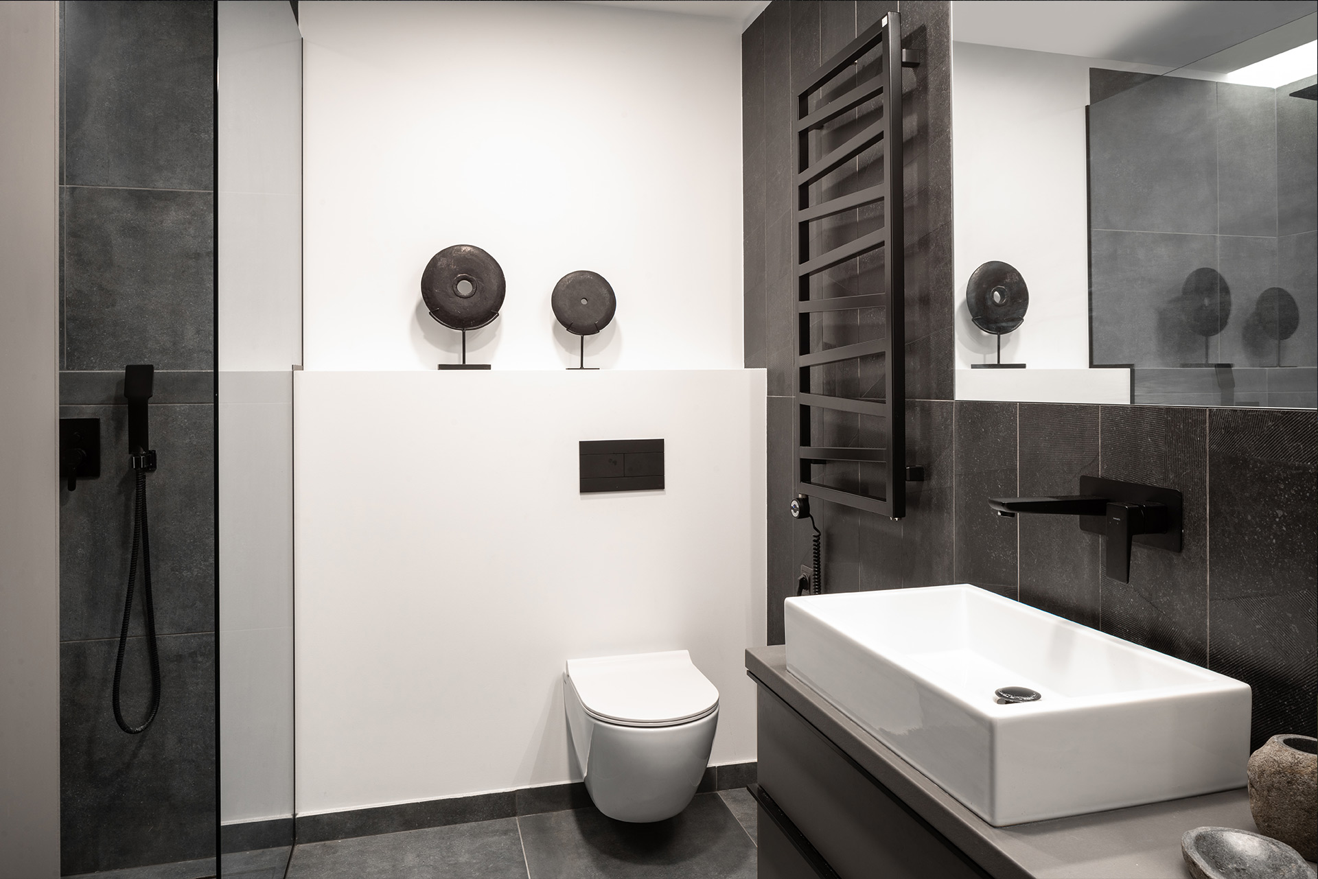 Modern bathroom with dark tiles and white sanitary ware — interior by TOMA Studio.