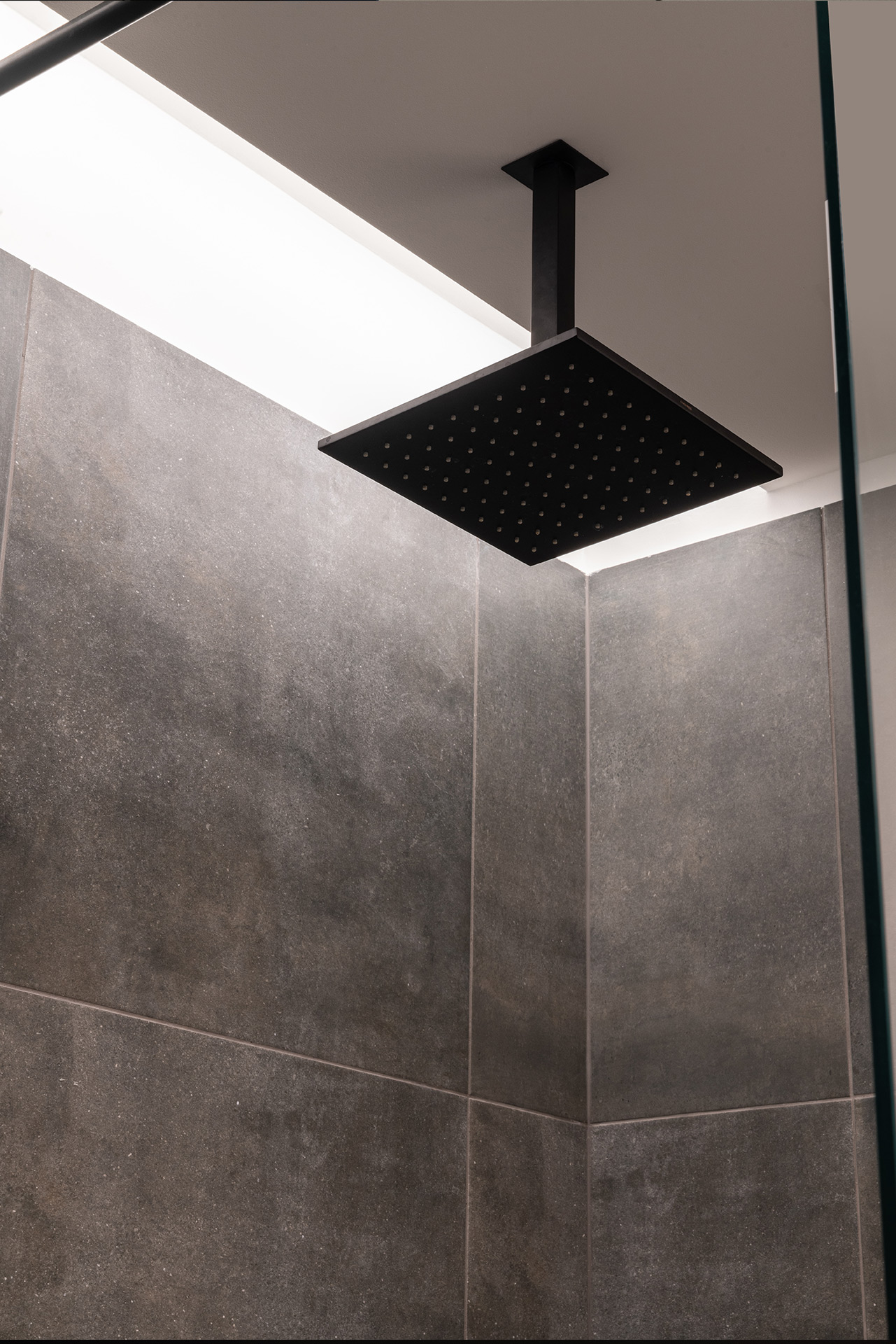 Ceiling-mounted square rain shower with grey textured wall tiles — interior by TOMA Studio.