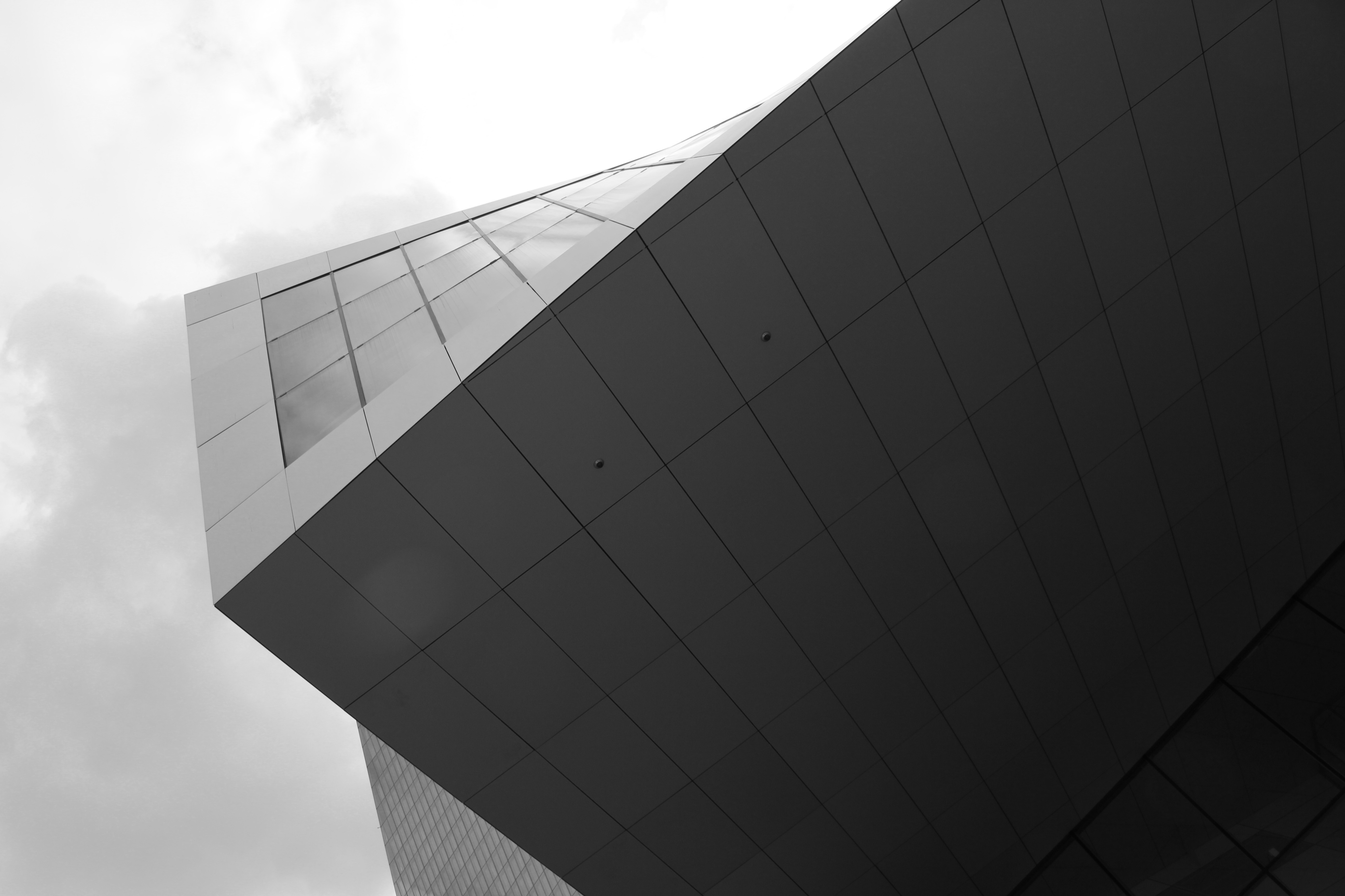 Minimal composition of a modern building corner with reflective glass and cloudy sky — architectural photography by TOMA Studio.