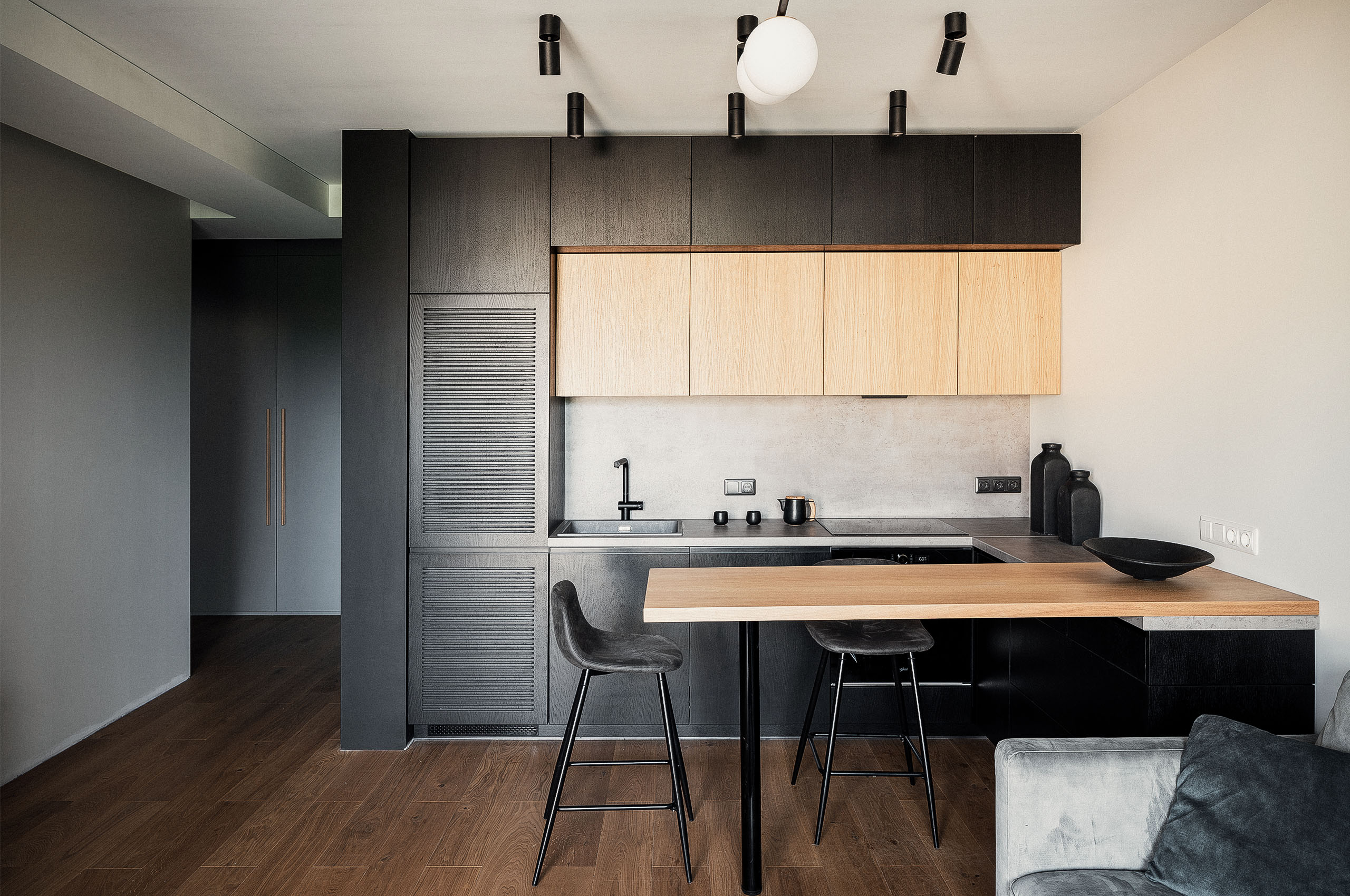 Moderne Küche mit schwarzen und Eichenholzschränken, Betonrückwand und einem kleinen Bartresen mit zwei Hockern.