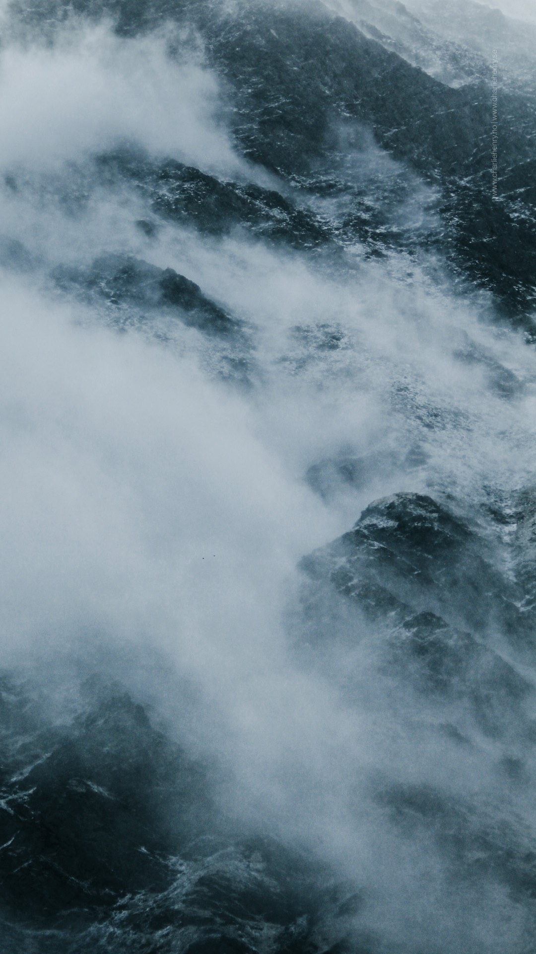 Dramatic close-up of mist and clouds swirling over dark, rugged mountain rocks in the Altai region — atmospheric landscape photography by Charlie Henry.