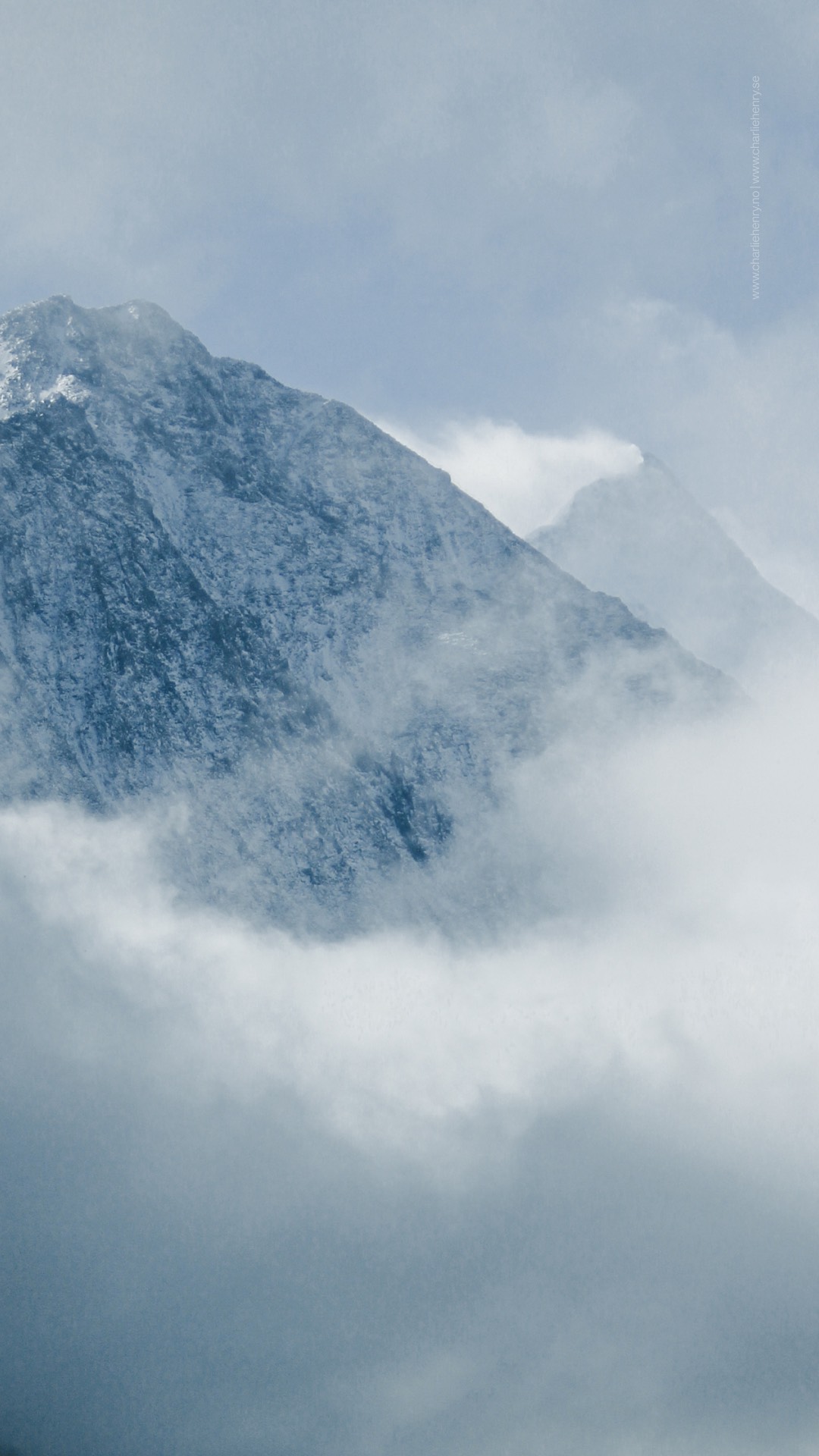 Blue-toned mountain peaks partially obscured by swirling clouds in the Altai region of Russia — atmospheric photography by Charlie Henry.