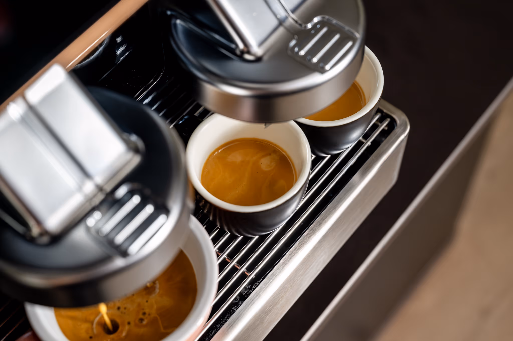 Close-up of a coffee machine brewing espresso into three black cups with white interiors.