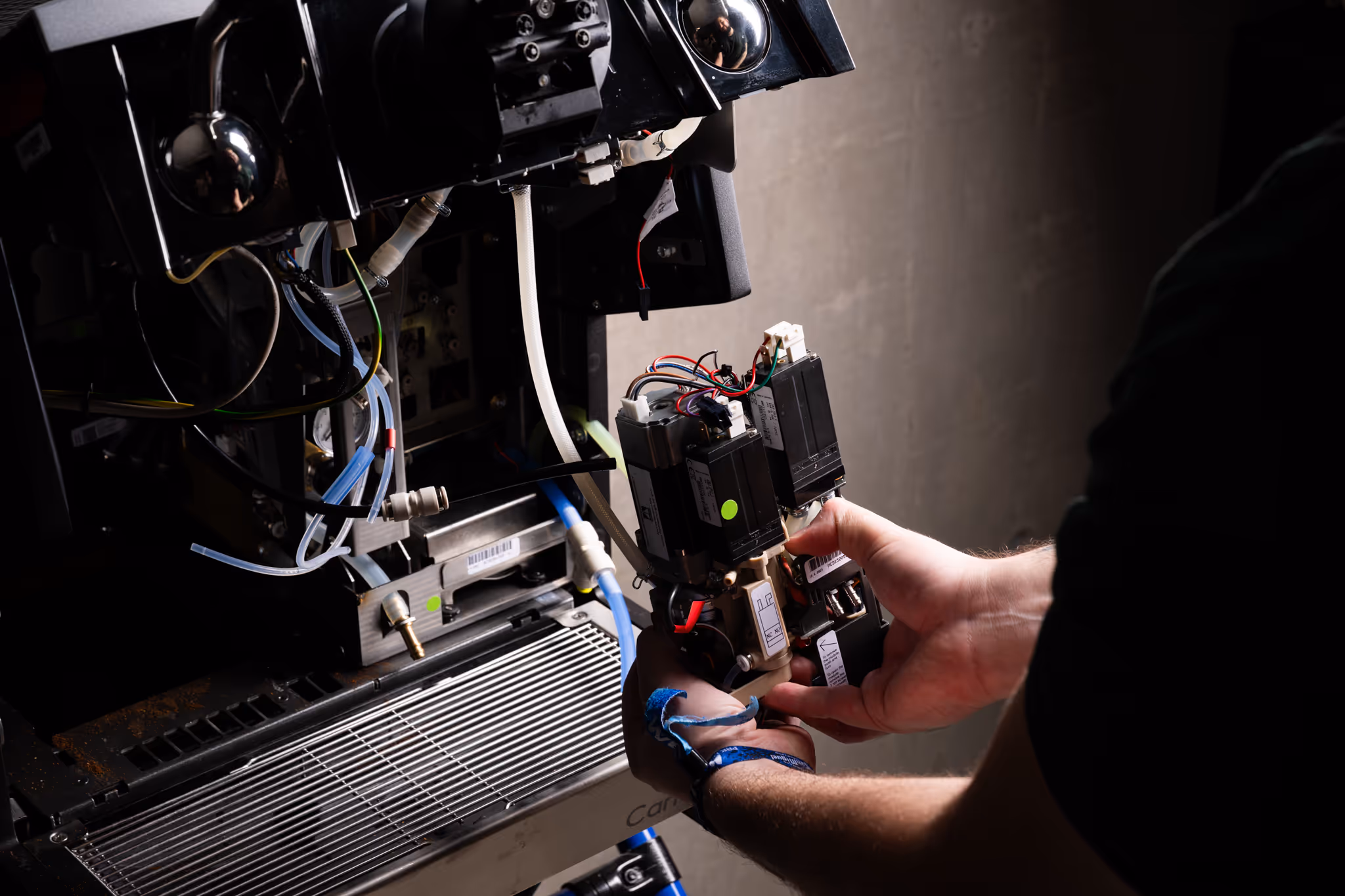 Person repairing or assembling the internal components of a coffee machine with visible wires and tubes.