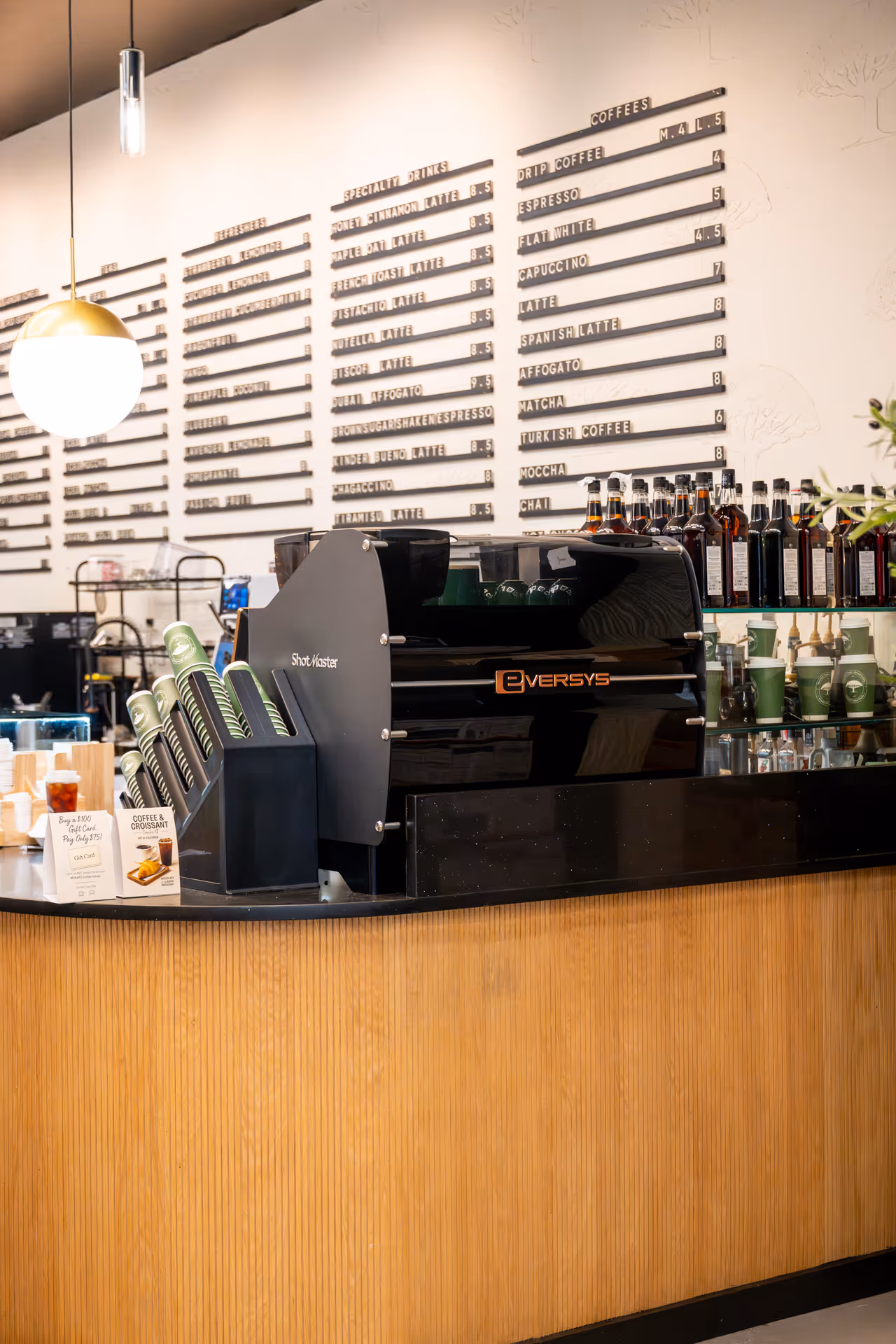Modern coffee shop counter with Eversys espresso machine, menu boards on the wall, and coffee syrup bottles.