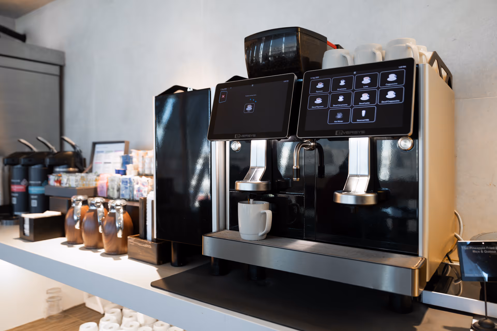 Modern black coffee machine with dual touchscreen displays dispensing coffee into a white mug on a countertop.