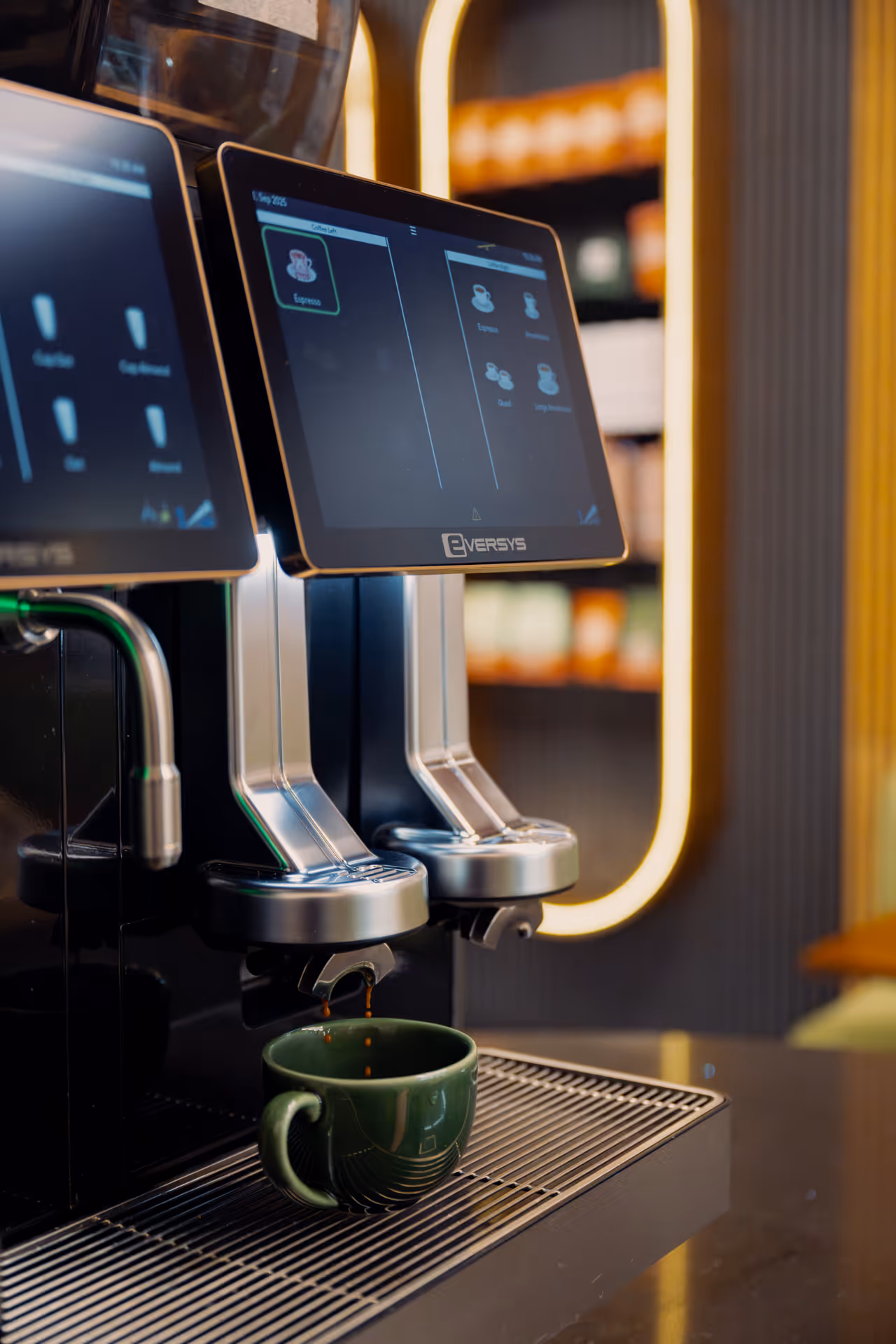 Automatic coffee machine dispensing espresso into a green ceramic cup on a drip tray.